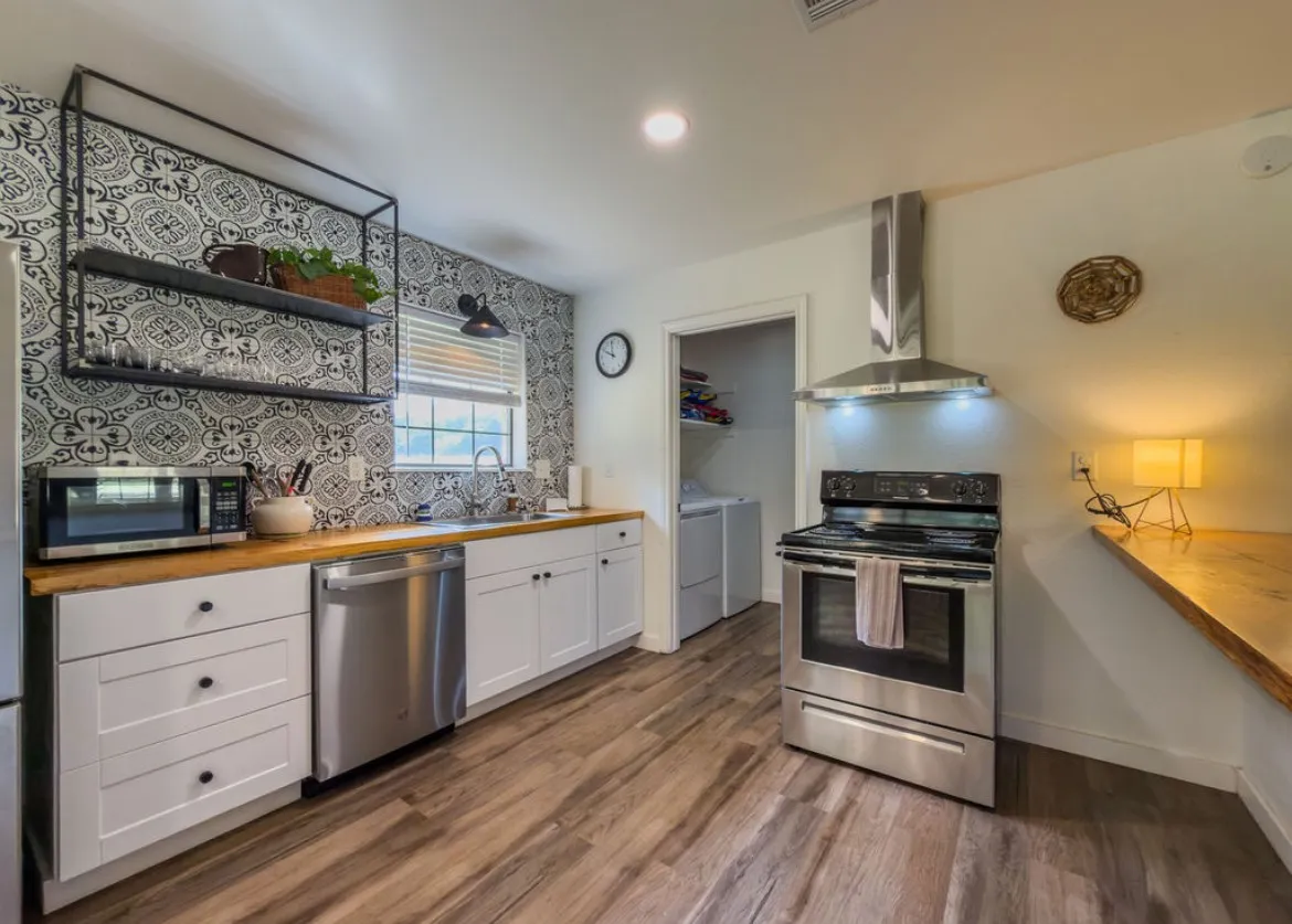 Wood-finish flooring, white cabinetry, stainless steel appliances, wood countertops, and a patterned tile backsplash