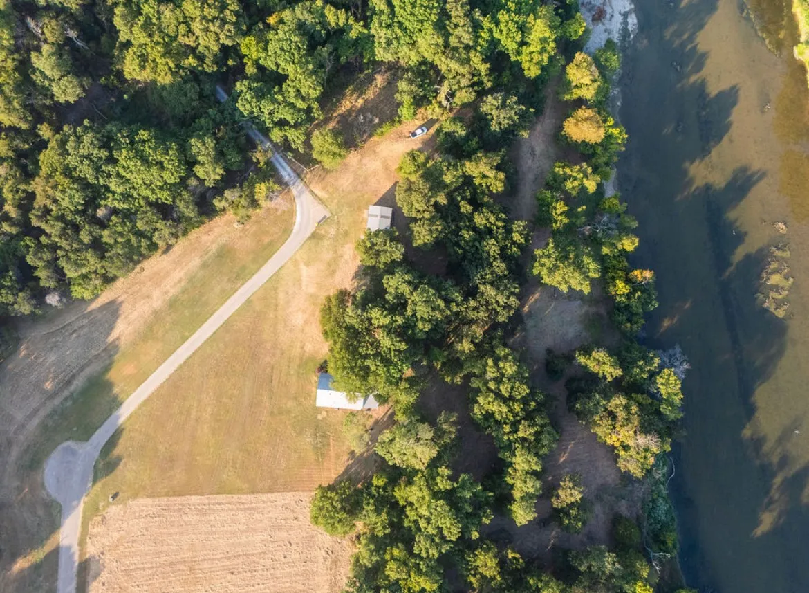 Expansive property with direct river frontage, featuring mature trees, open grassy areas, and a paved access road