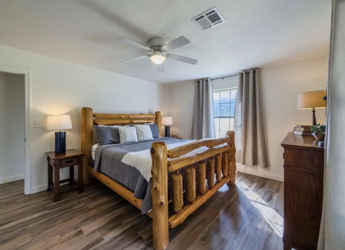 Spacious room featuring wood-finish flooring, a ceiling fan, and window with drapes