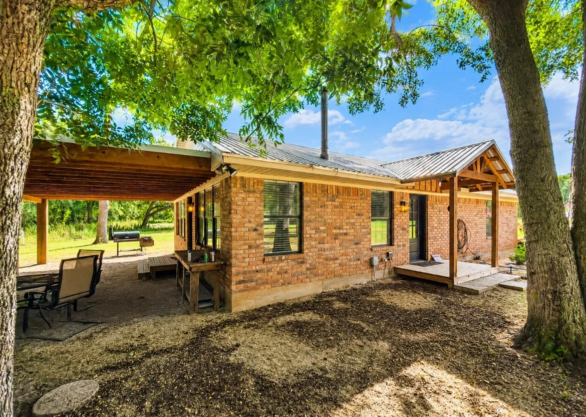 Brick exterior featuring multiple windows with blinds, a covered patio with a wood ceiling, and a covered entry porch with wood columns