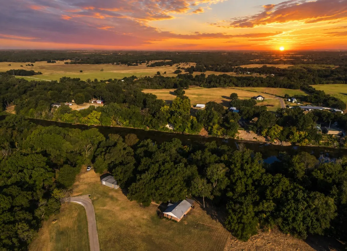 Expansive land featuring mature trees, a winding river, open fields, and distant structures