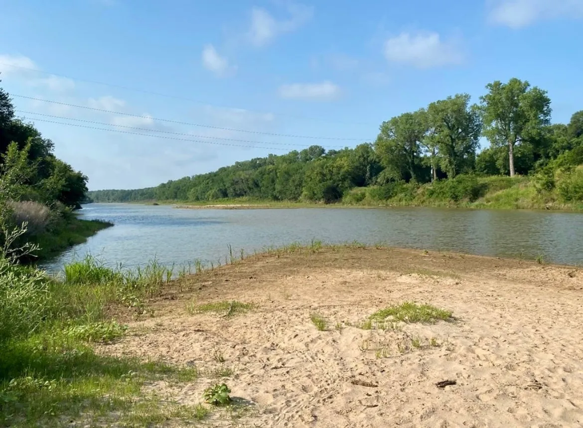 Sandy shore with natural river frontage, surrounded by mature trees and lush greenery