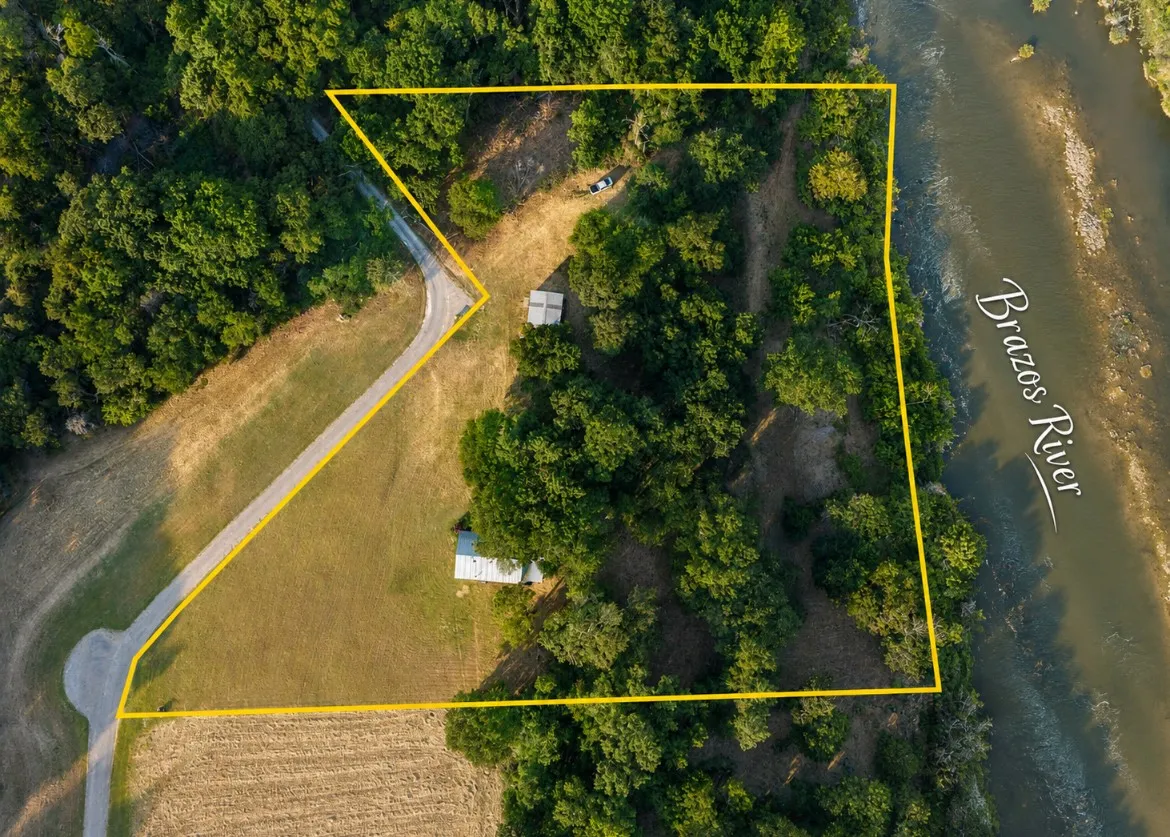 Extensive acreage with a defined property line, direct river frontage, natural tree cover, a private driveway, and a visible structure