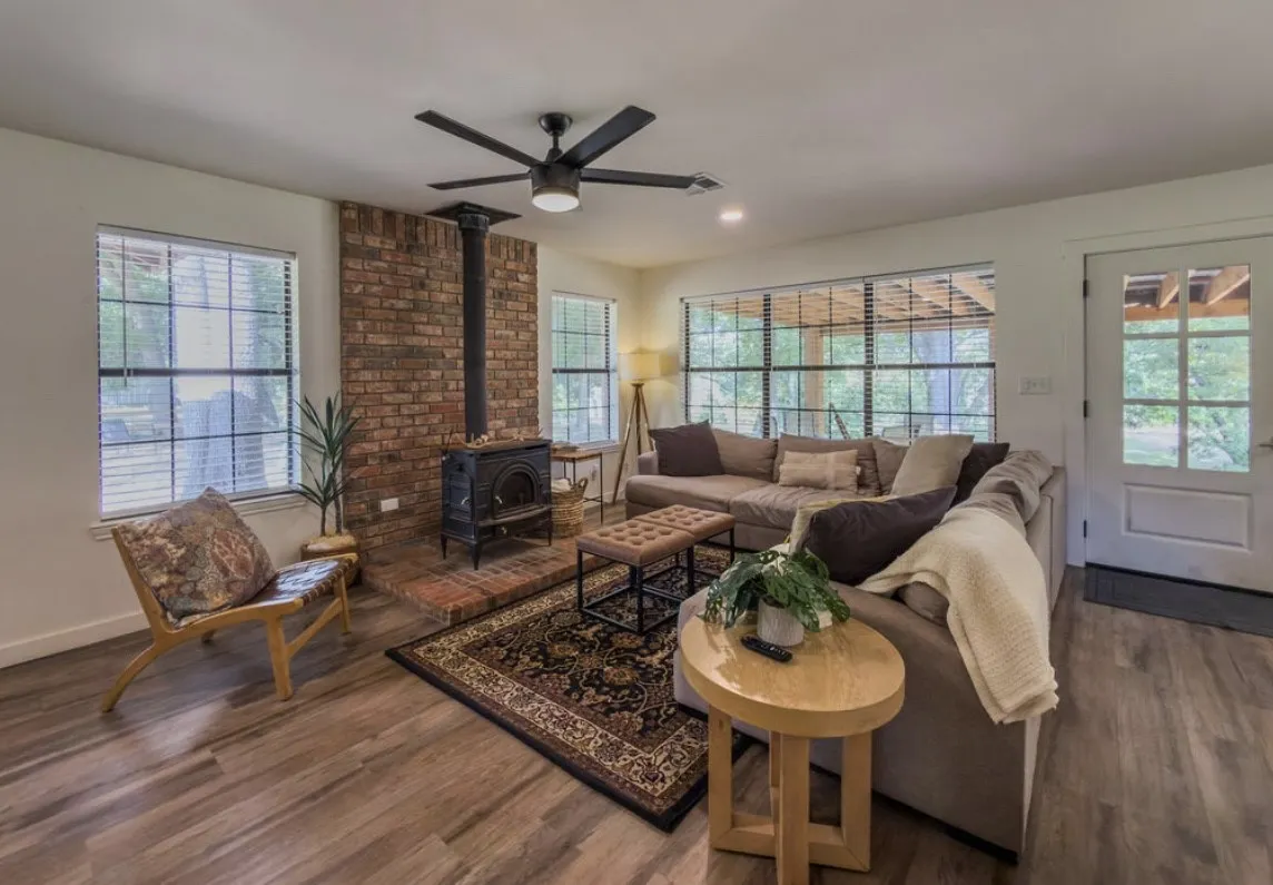 Wood-finish flooring, brick-clad fireplace, black ceiling fan, recessed lighting, and a glass-paned exterior door