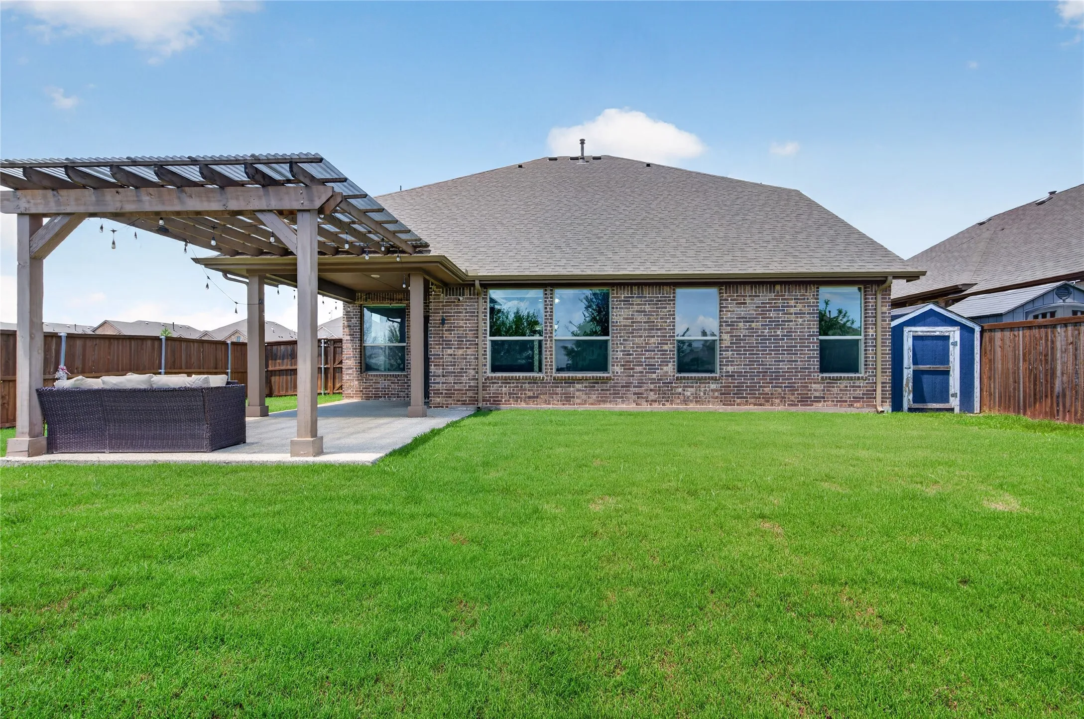 Expansive backyard featuring a manicured lawn, brick exterior, covered patio, and a wood pergola