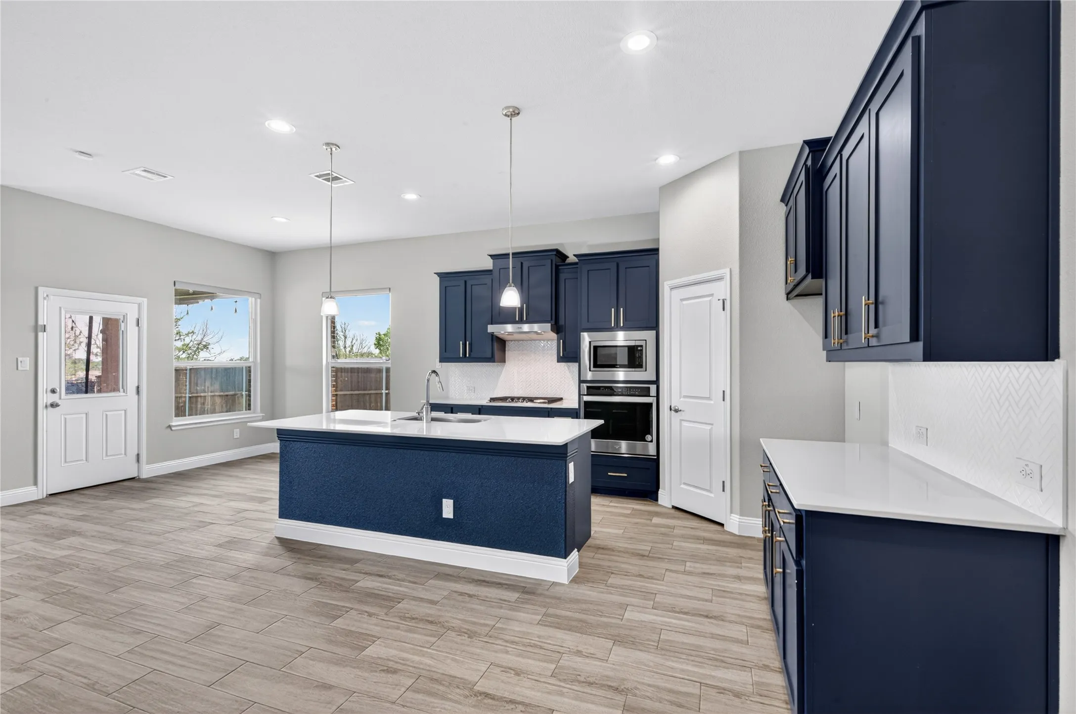 Spacious kitchen featuring dark blue cabinetry, light countertops, wood-finish flooring, stainless steel appliances, and pendant lighting