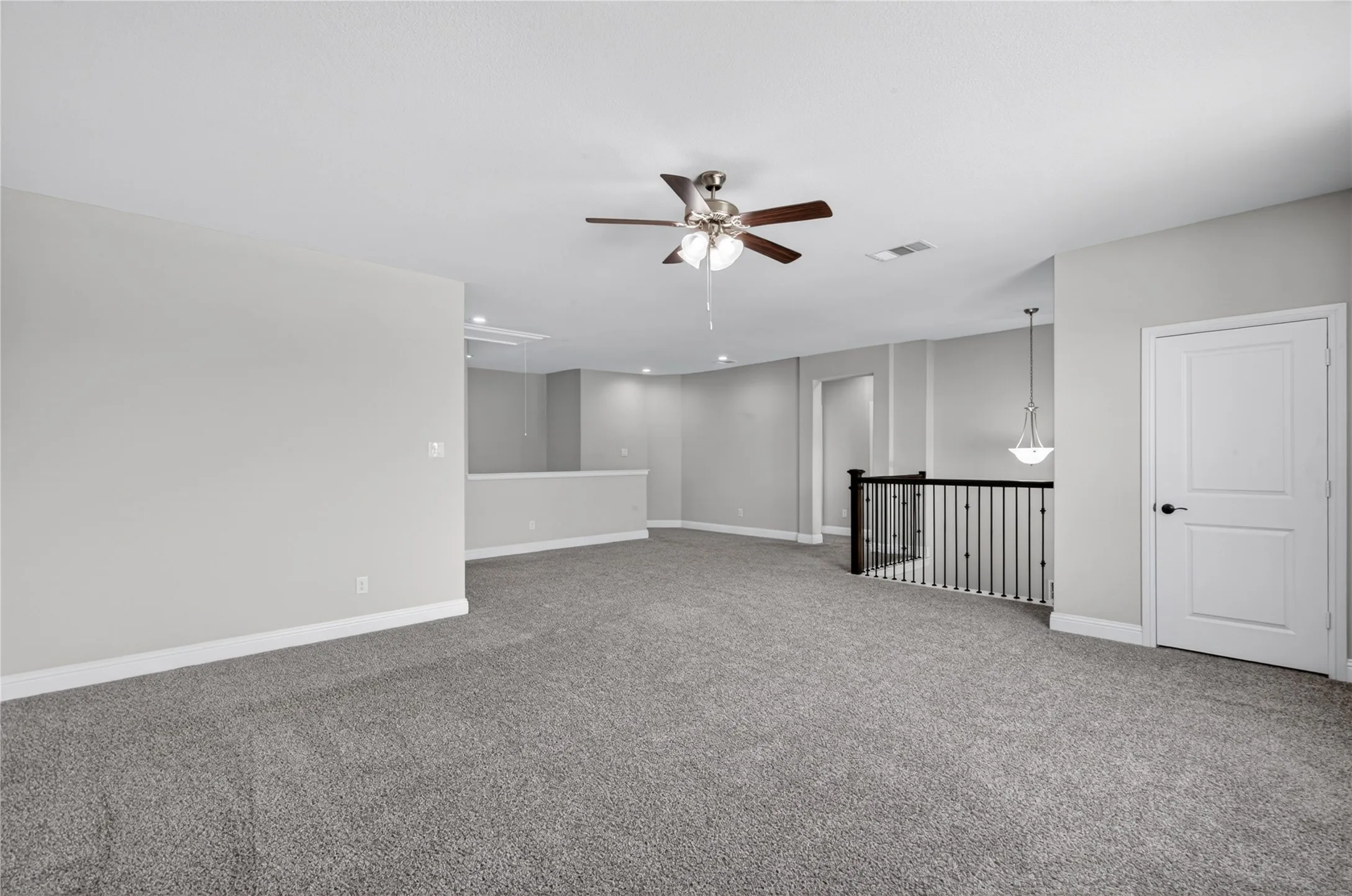 Spacious carpeted area with a ceiling fan, recessed lighting, and a white paneled door