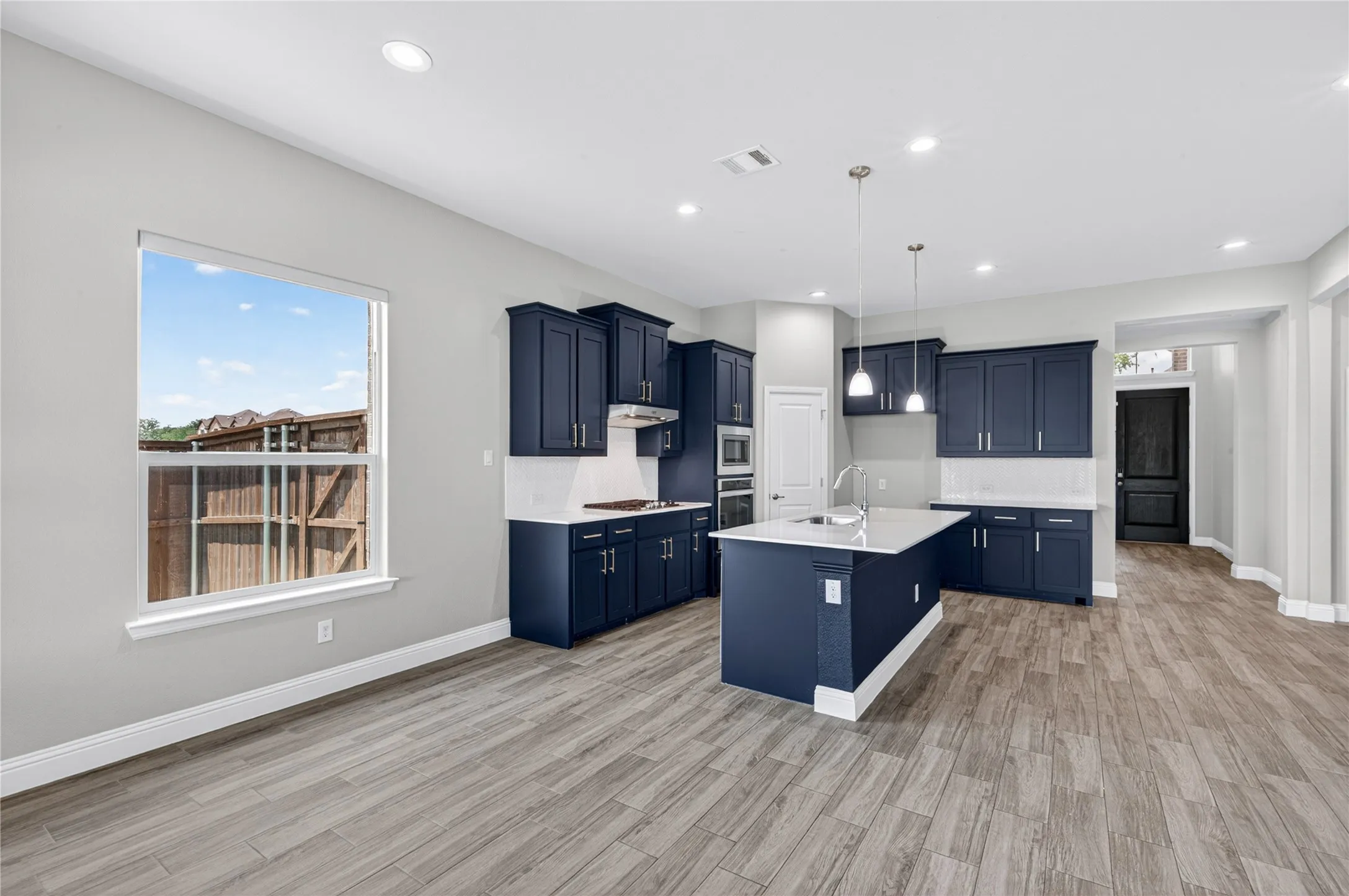 Open-concept kitchen featuring dark blue cabinetry, light countertops, a central island with a sink, pendant lighting, and wood-finish flooring