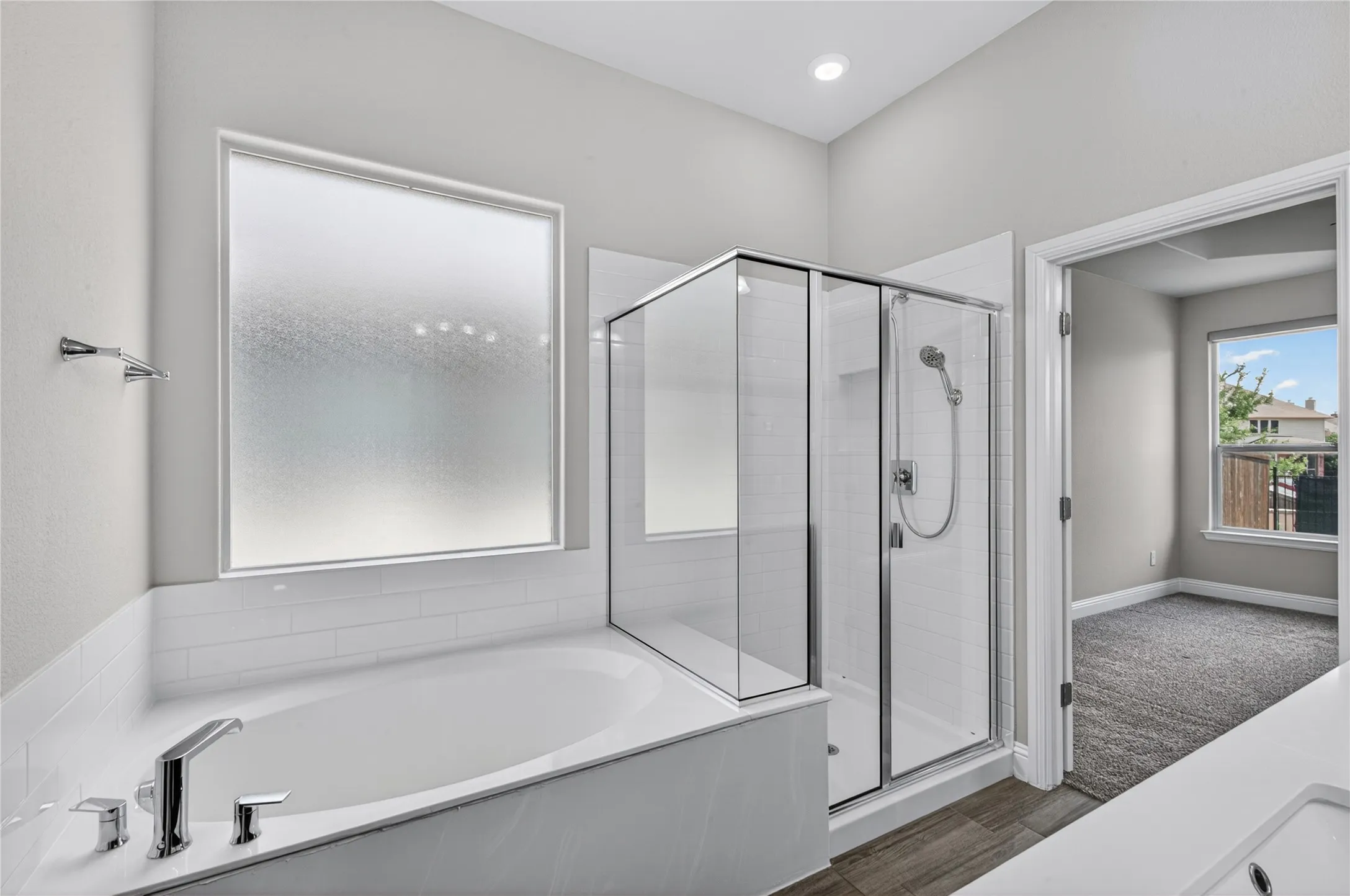 Soaking tub with chrome fixtures, glass-enclosed shower, wood-finish flooring, and recessed ceiling lighting