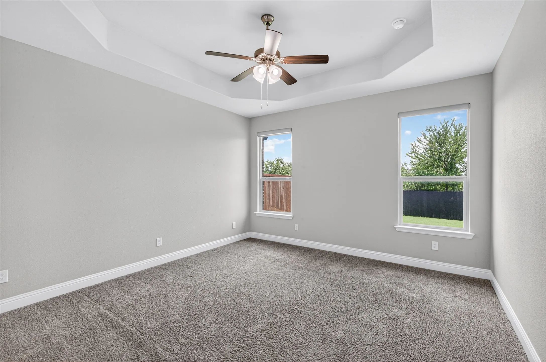 Tray ceiling with recessed lighting and a ceiling fan, dual windows, and plush carpet flooring