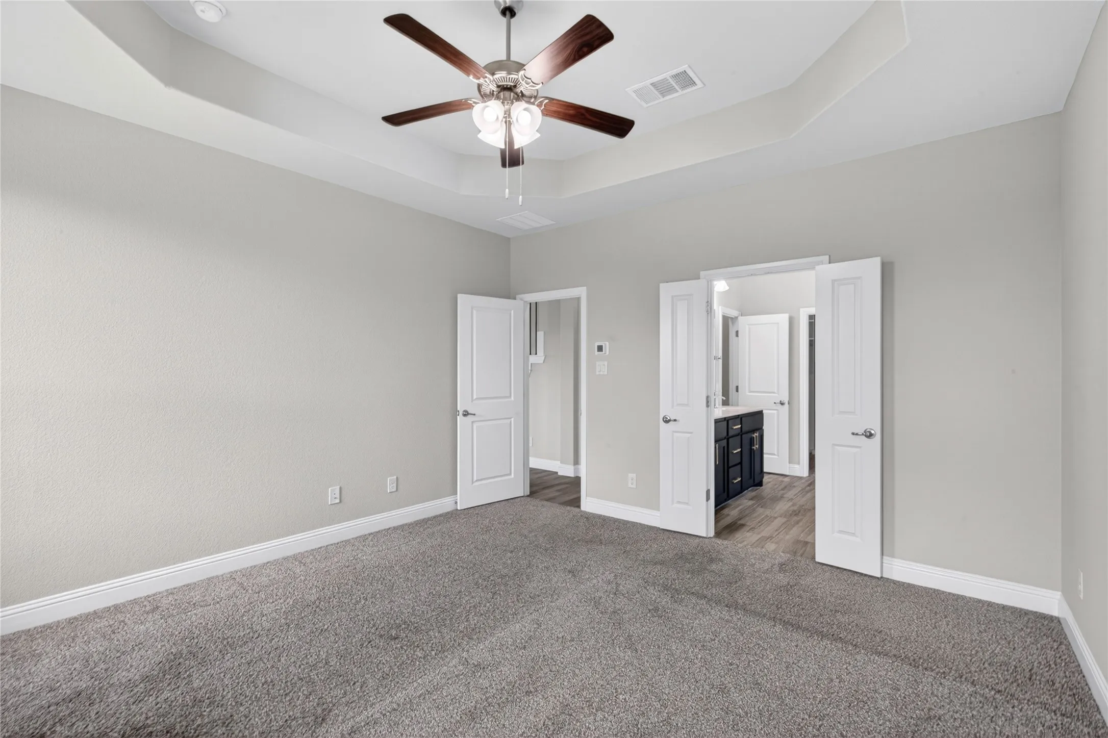 Tray ceiling with a ceiling fan, light gray wall finishes, gray carpet flooring, and white paneled doors
