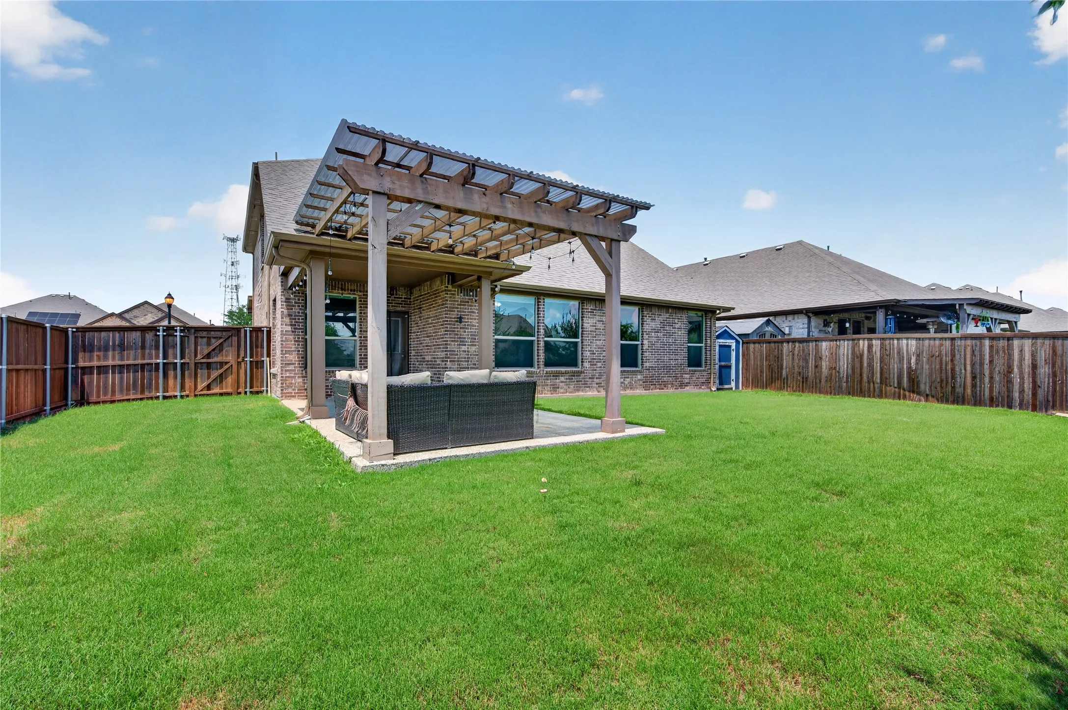 Expansive grassy yard with a covered patio, wood pergola, and brick exterior