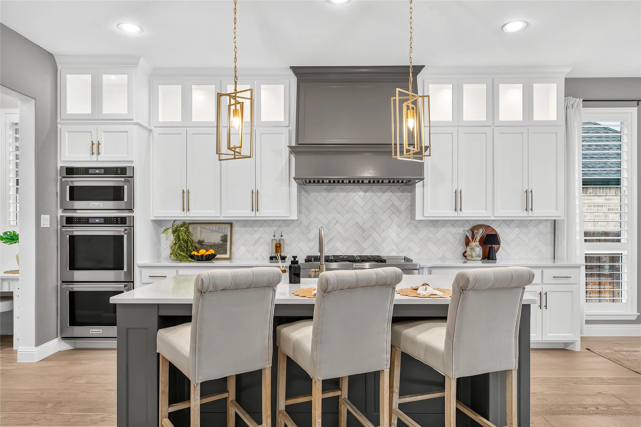 Chef-inspired kitchen features a statement hood, gold pendant lighting, quartz countertops, floor to ceiling cabinets, double oven and gas cooktop.