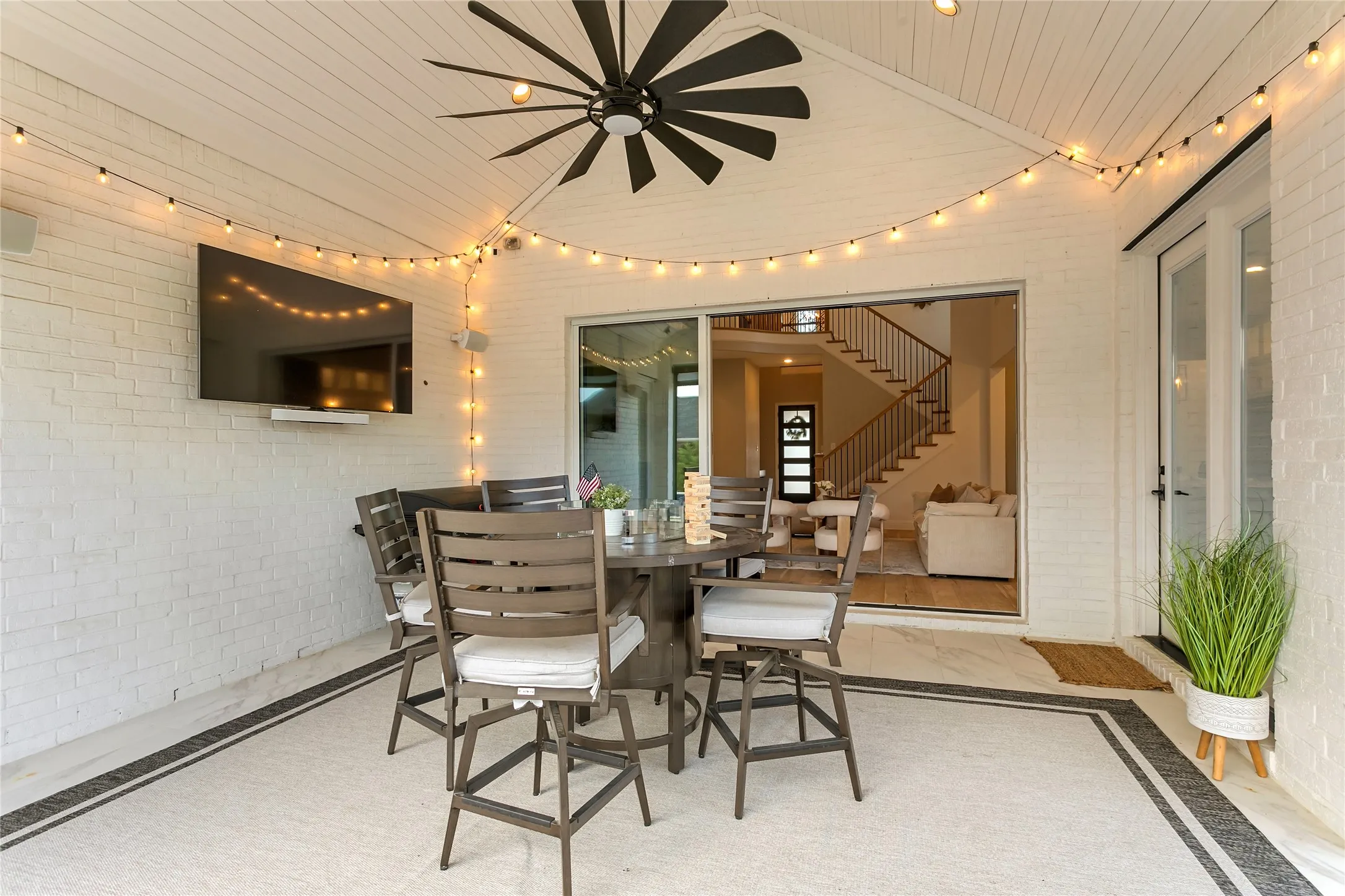 String-lit covered patio with a mounted TV and ceiling fan extends the living space outdoors.