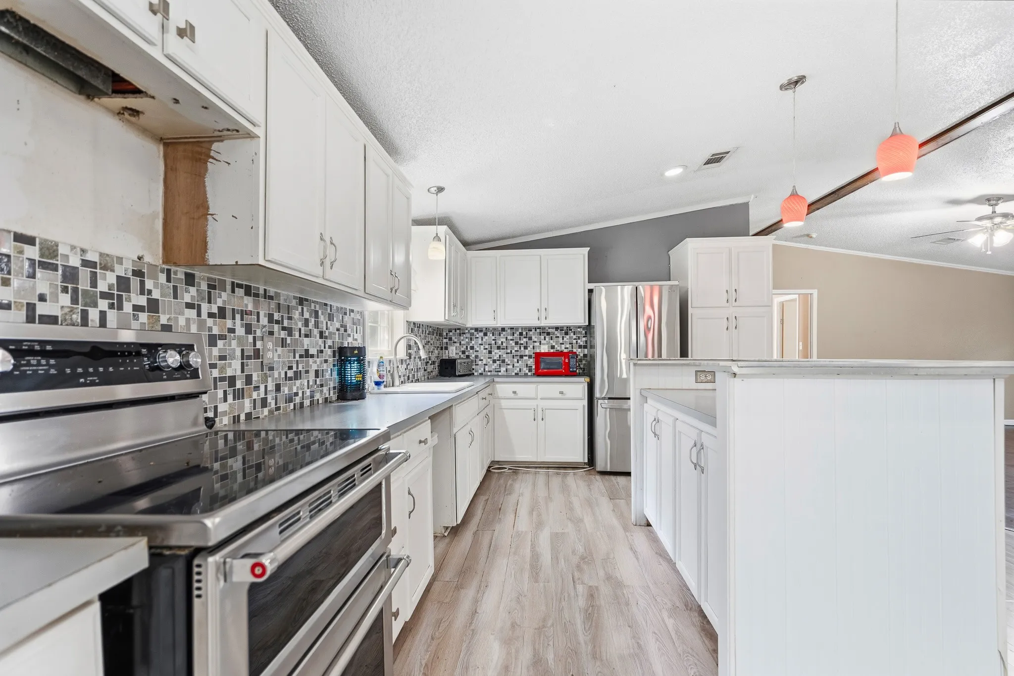White cabinetry with stainless steel appliances, mosaic tile backsplash, and light wood-finish flooring