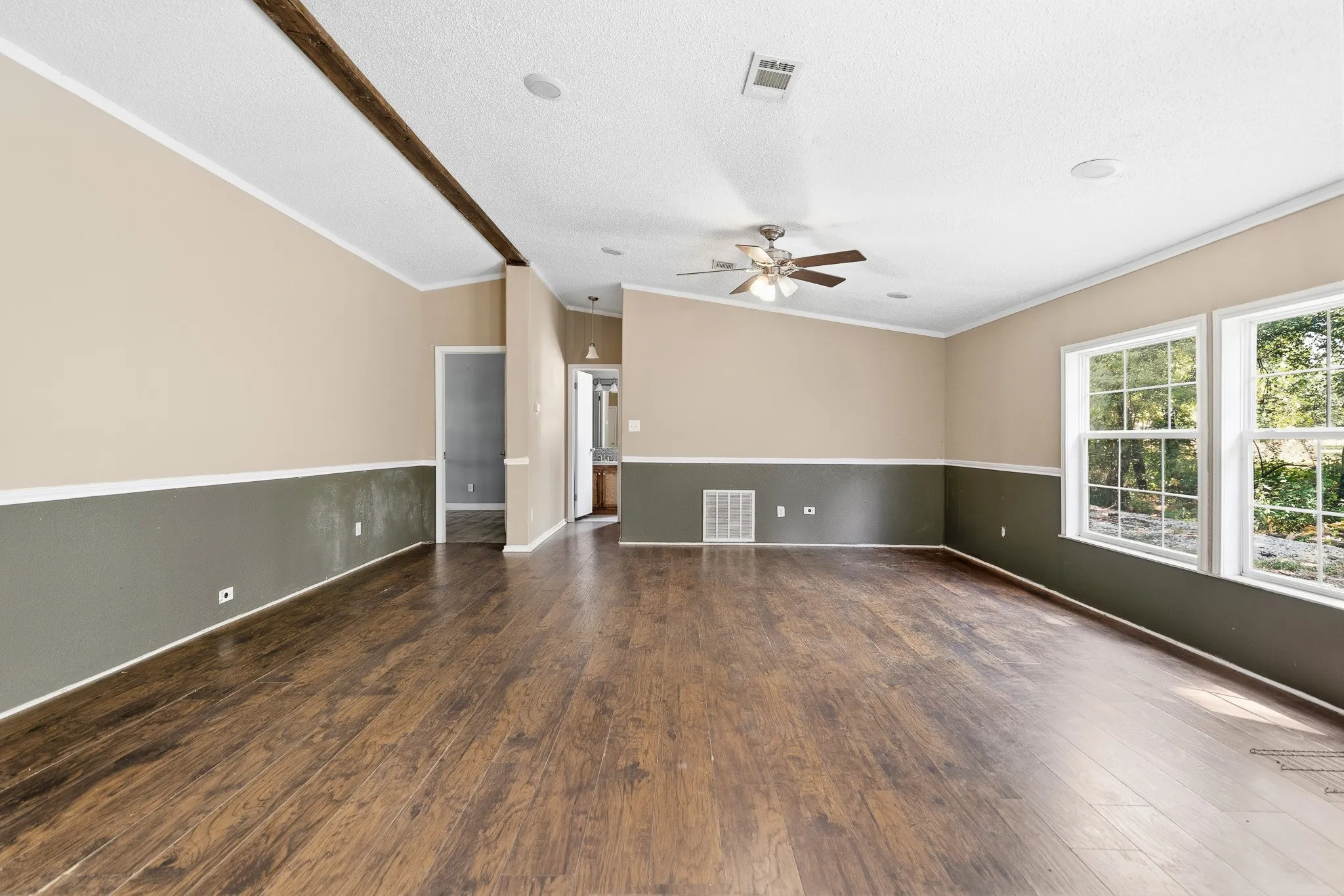 Spacious room featuring wood-finish flooring, a vaulted ceiling with a decorative beam, and a ceiling fan