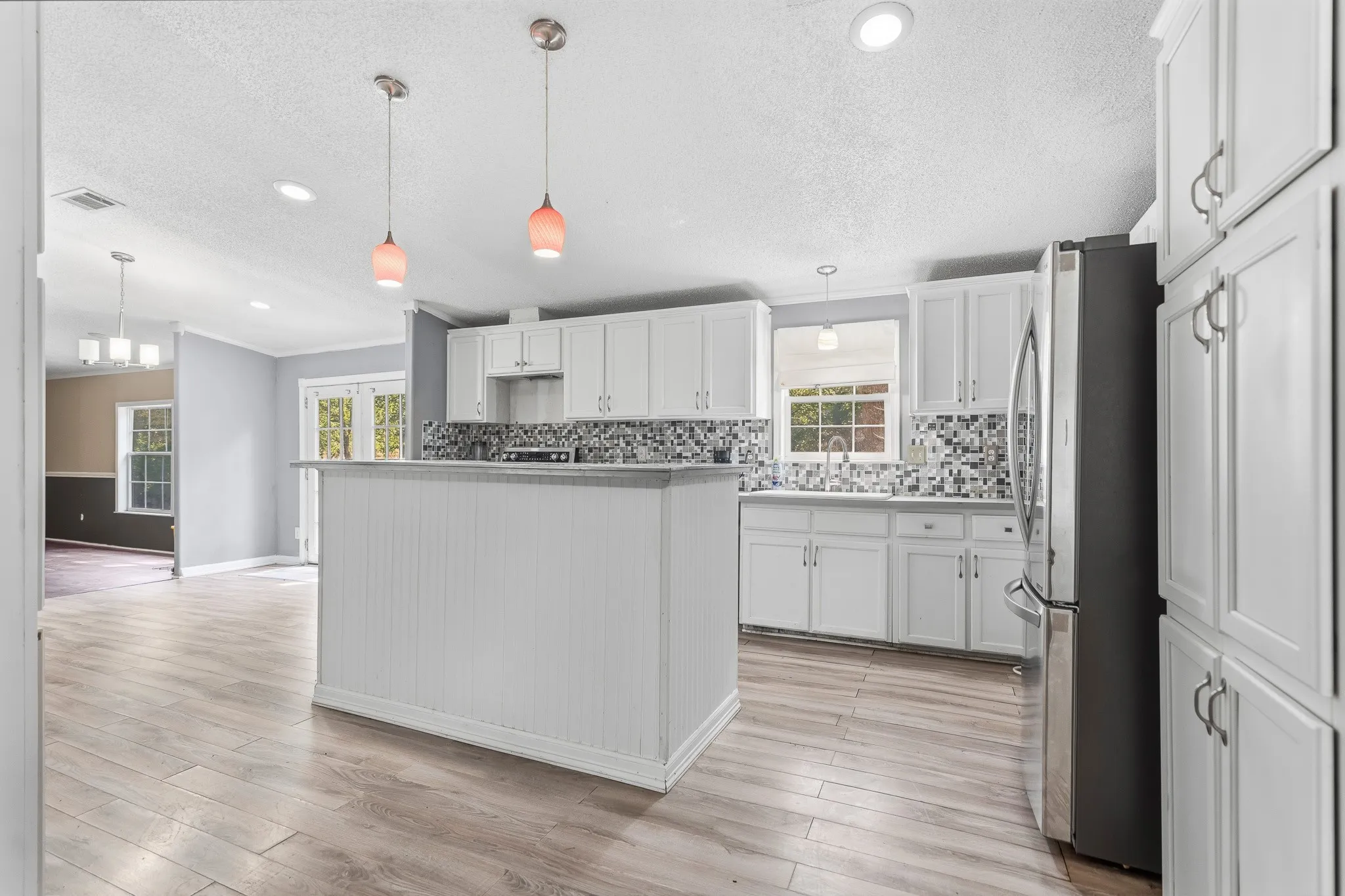 Kitchen featuring white shaker cabinetry, stainless steel appliances, mosaic tile backsplash, wood-finish flooring, and a central island with beadboard paneling