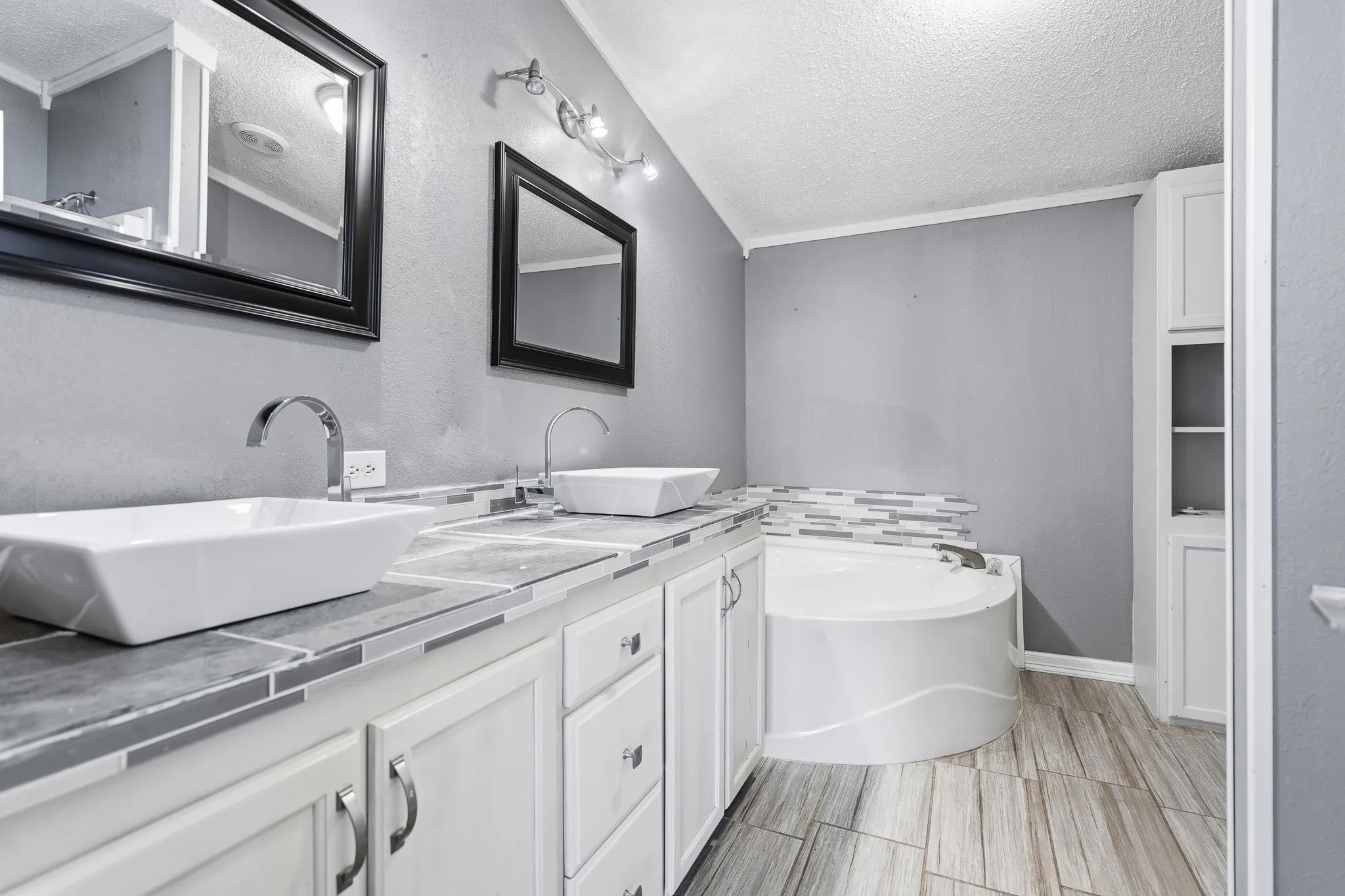 Dual vessel sinks, white cabinetry, tile countertop, corner soaking tub, and tile flooring
