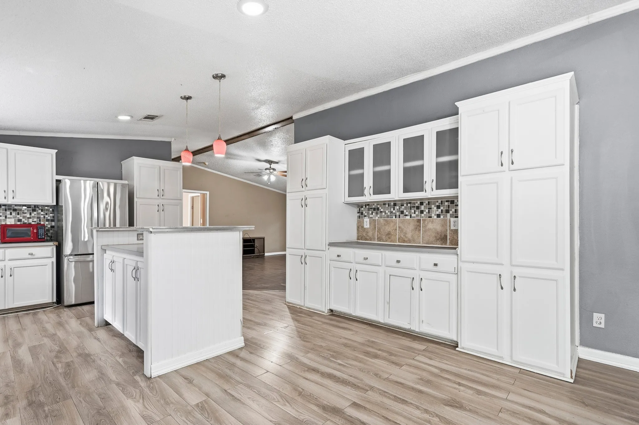 Spacious kitchen featuring extensive white cabinetry, a center island with countertop, stainless steel appliances, and wood-finish flooring