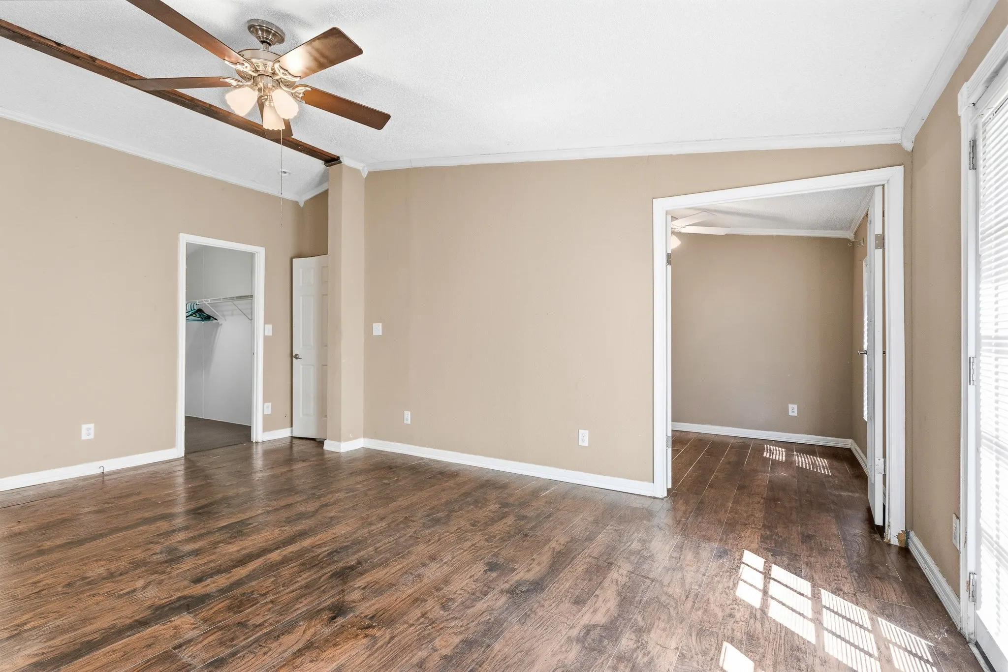 Wood-finish flooring throughout, ceiling fan with light fixture, and crown molding