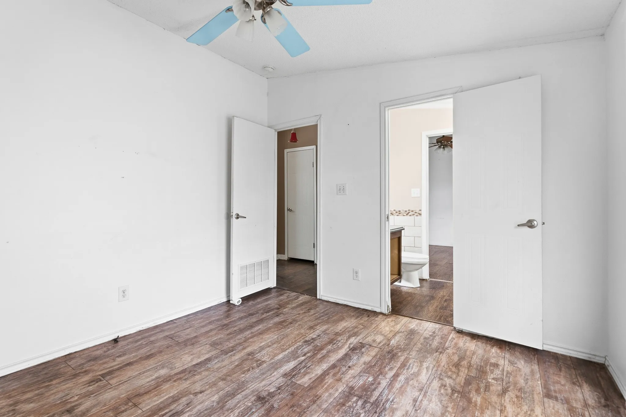 Wood-finish flooring throughout, bright white walls, and a ceiling fan with light fixture
