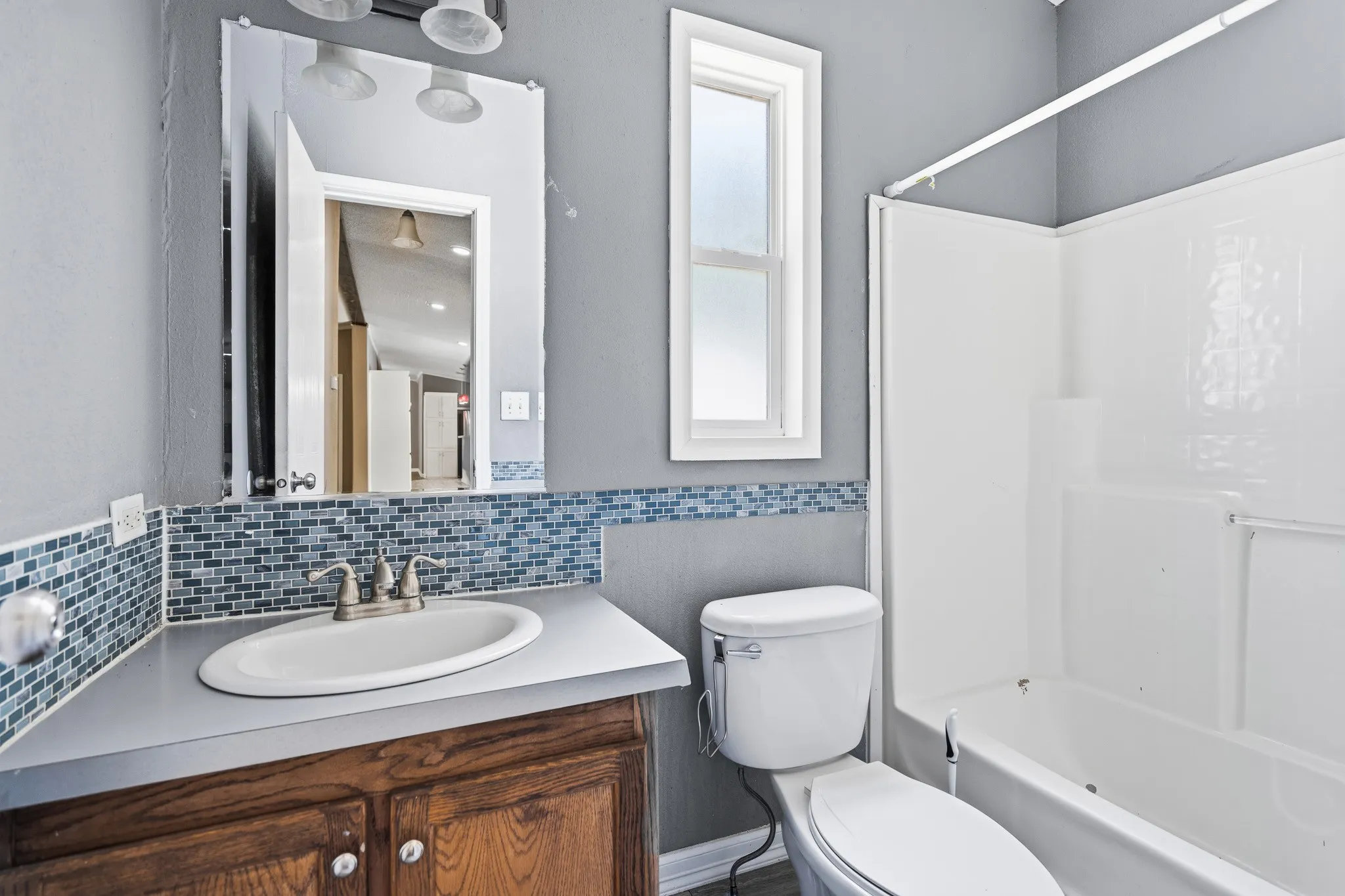 Wood-finish vanity with an oval sink, brushed nickel faucet, and mosaic tile backsplash