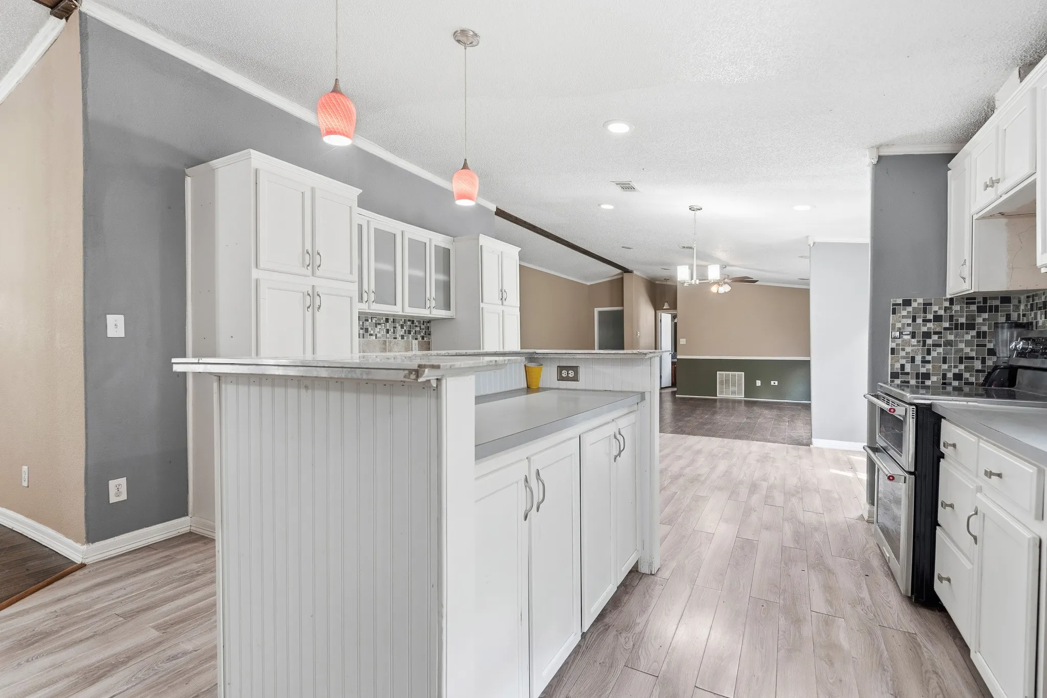 White cabinetry, wood-finish flooring, mosaic tile backsplash, double wall oven, and peninsula countertop