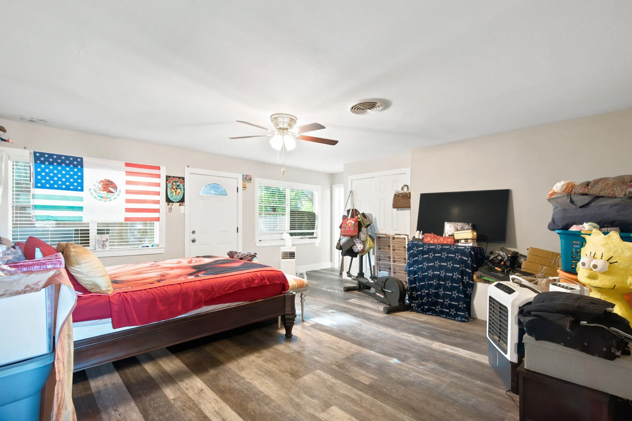 Wood-finish flooring throughout, multiple windows providing natural light, ceiling fan with integrated lighting, and a white paneled door with an arched glass insert