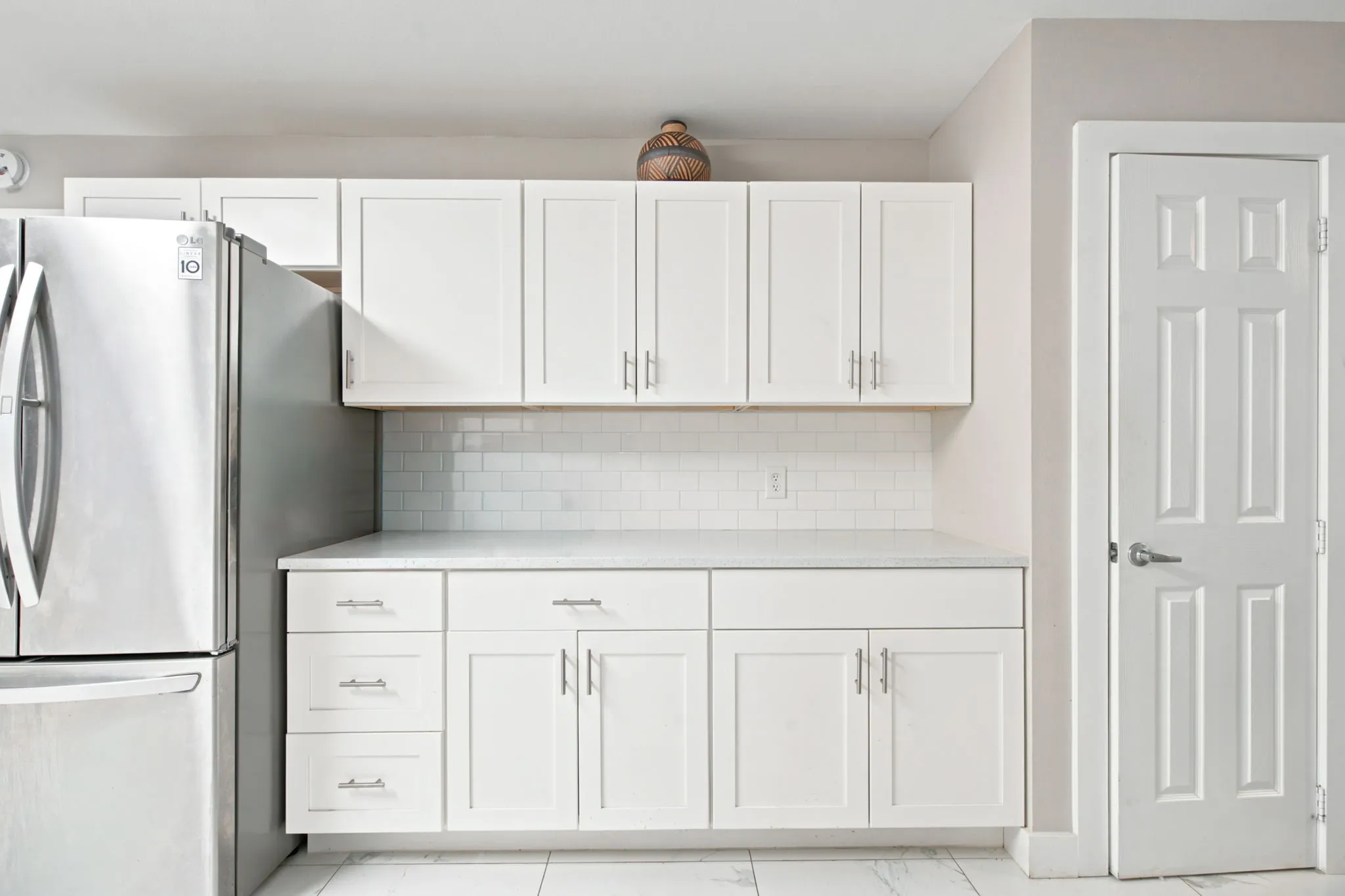 White shaker cabinetry, white subway tile backsplash, stainless steel refrigerator, white countertops, and a paneled interior door