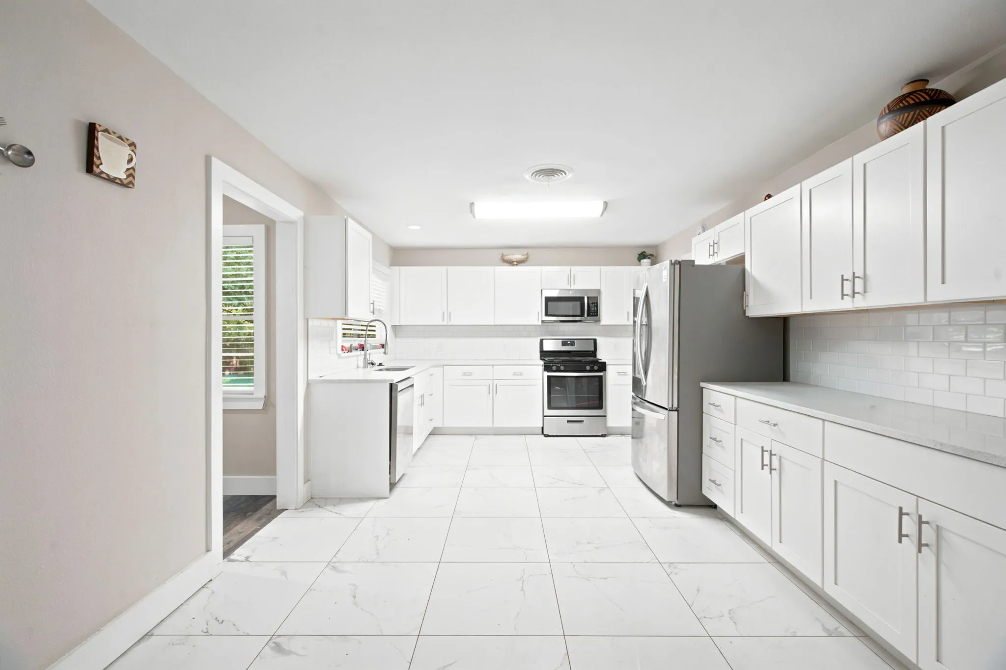 Spacious kitchen featuring white cabinetry, stainless steel appliances, light-toned countertops, subway tile backsplash, and large format tile flooring