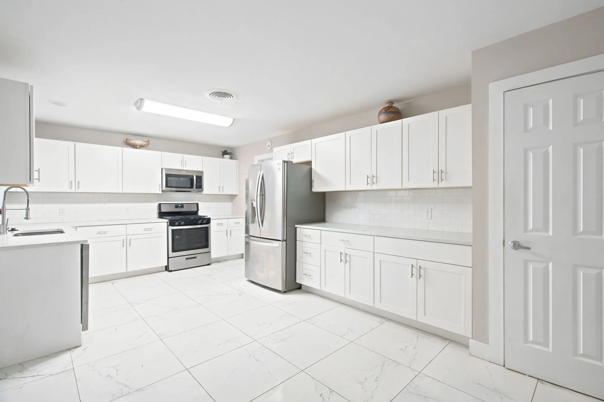 Kitchen featuring white shaker-style cabinetry, stainless steel appliances, a white tile backsplash, and light-colored flooring