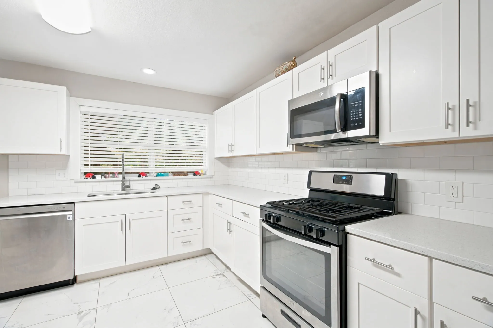 Modern kitchen featuring white shaker cabinetry, stainless steel appliances, white subway tile backsplash, light countertops, and large format floor tiles