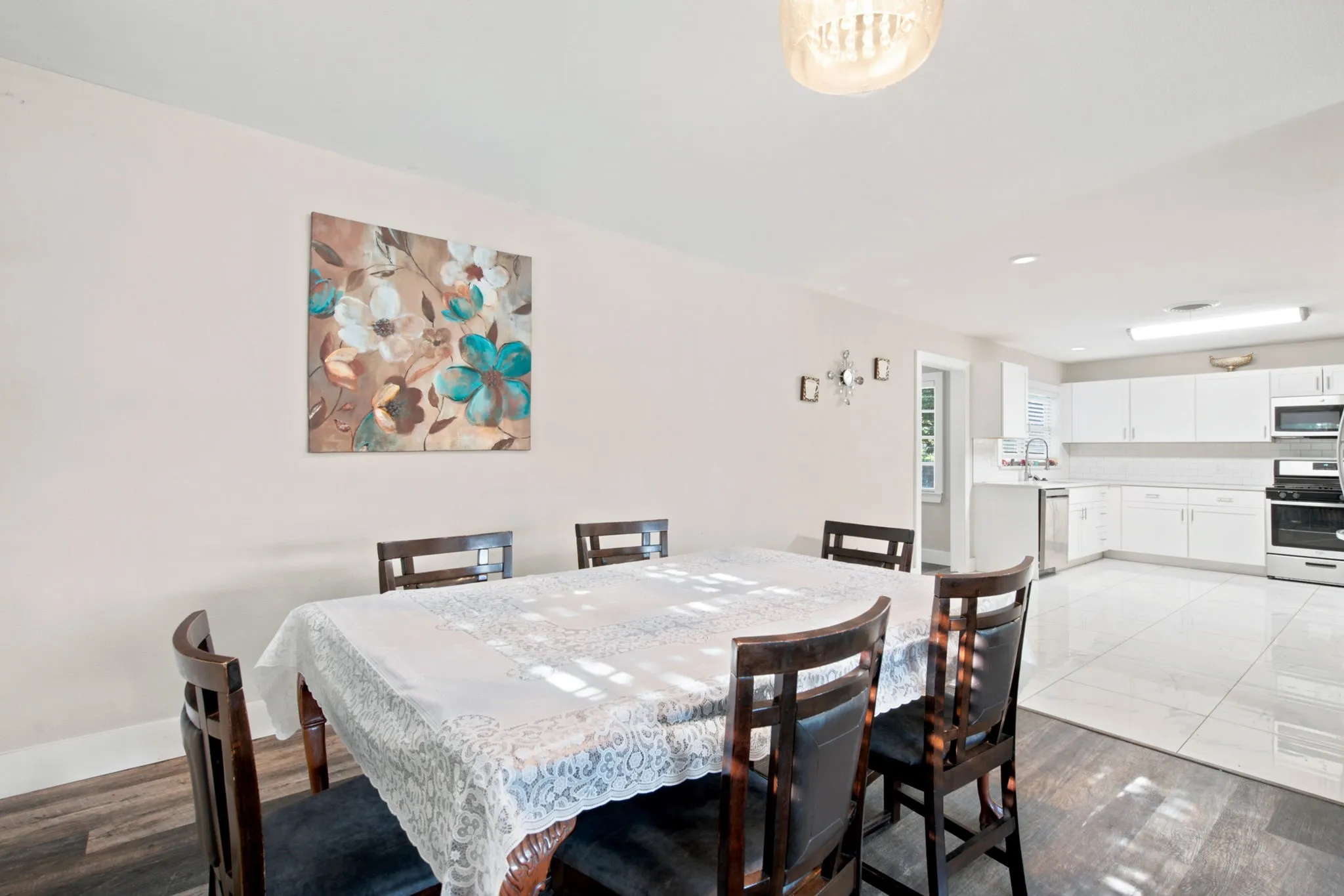 Wood-finish flooring in the dining area, white tile flooring in the kitchen, white kitchen cabinetry, stainless steel appliances, and a built-in kitchen sink