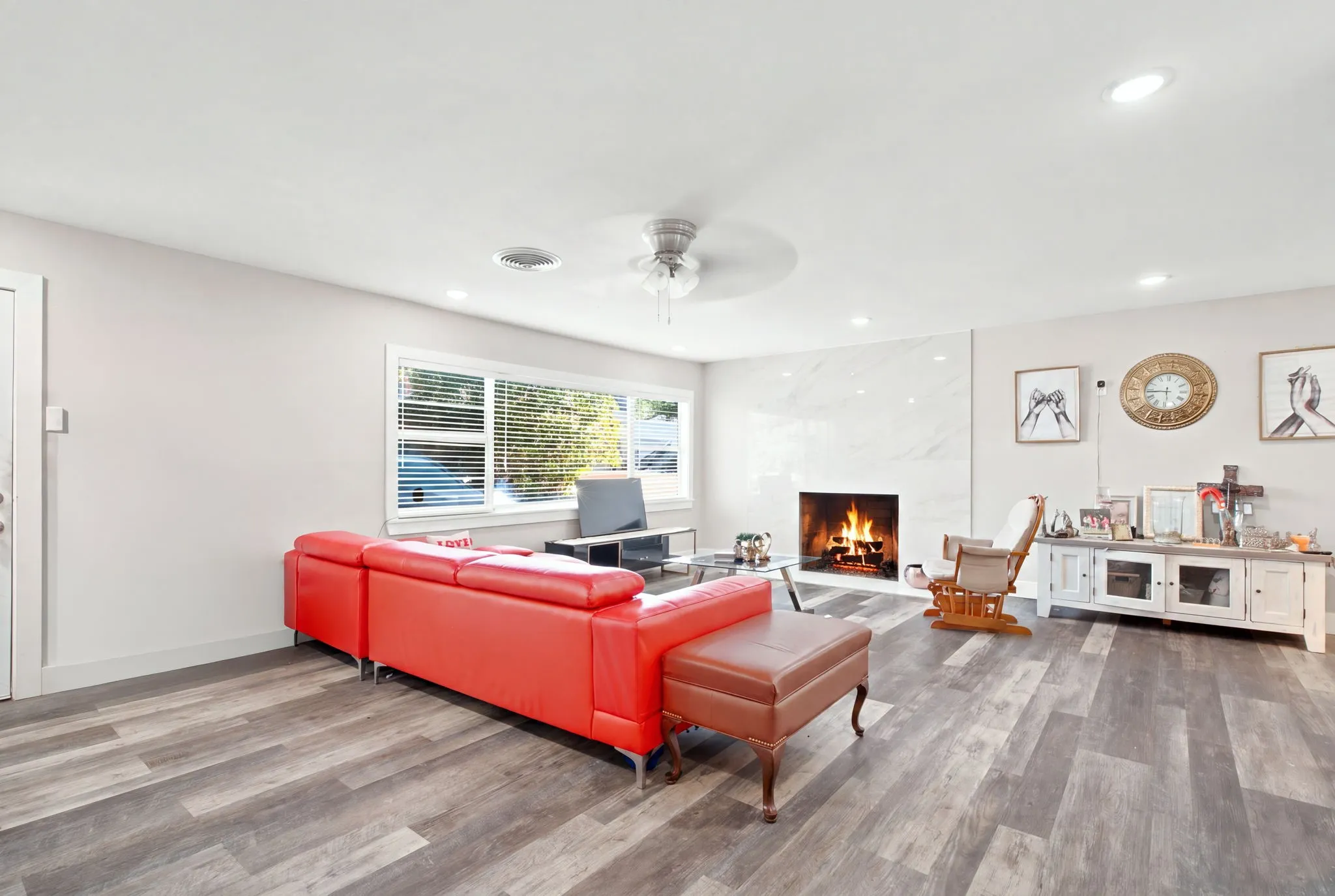 Spacious living area featuring wood-finish flooring, a contemporary fireplace with a stone surround, recessed lighting, a ceiling fan, and large windows with blinds