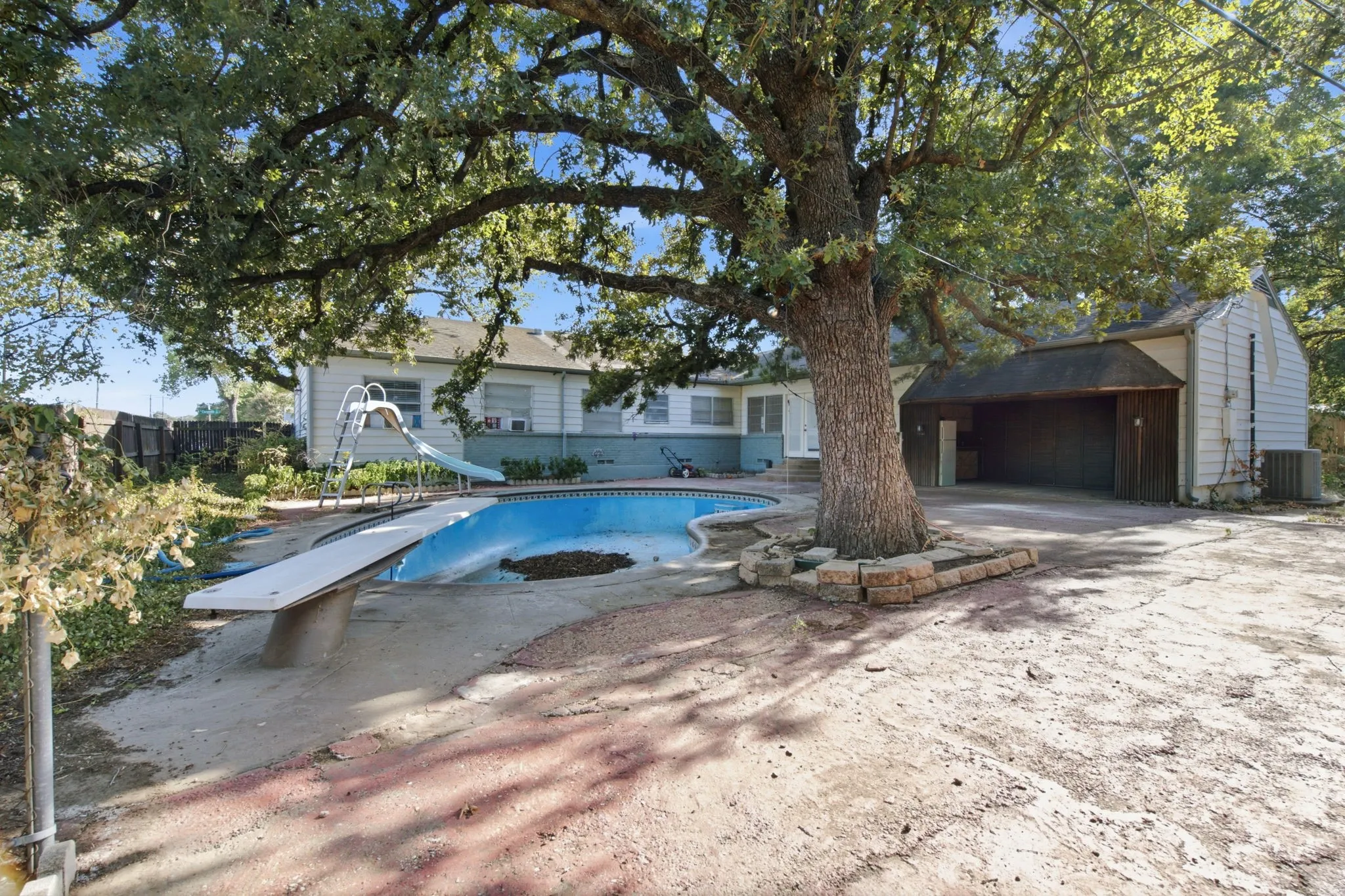 In-ground swimming pool with diving board, mature tree, and detached covered parking structure