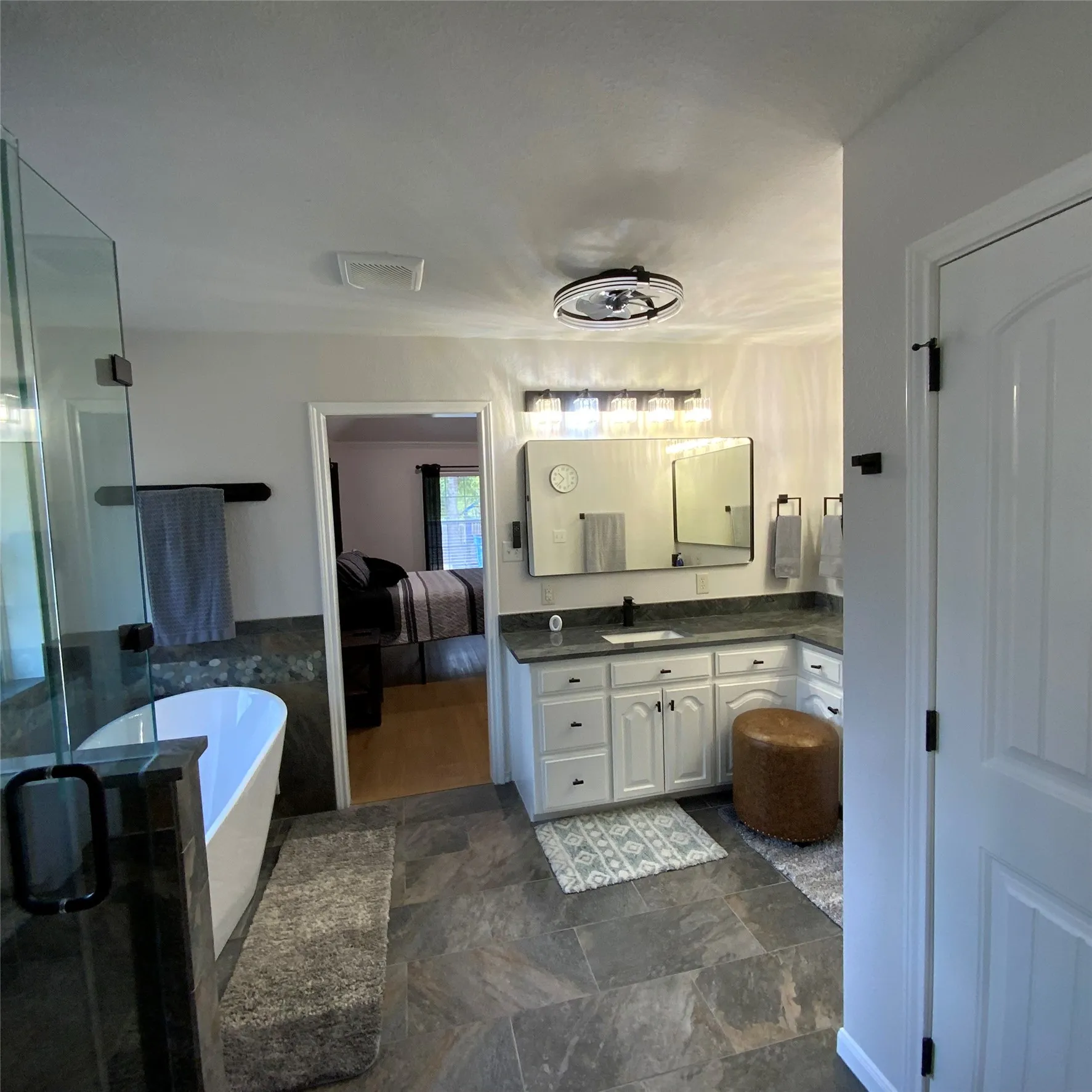 Large format tile flooring, freestanding soaking tub, glass-enclosed shower, dual vanity with undermount sinks, and a framed mirror with integrated lighting