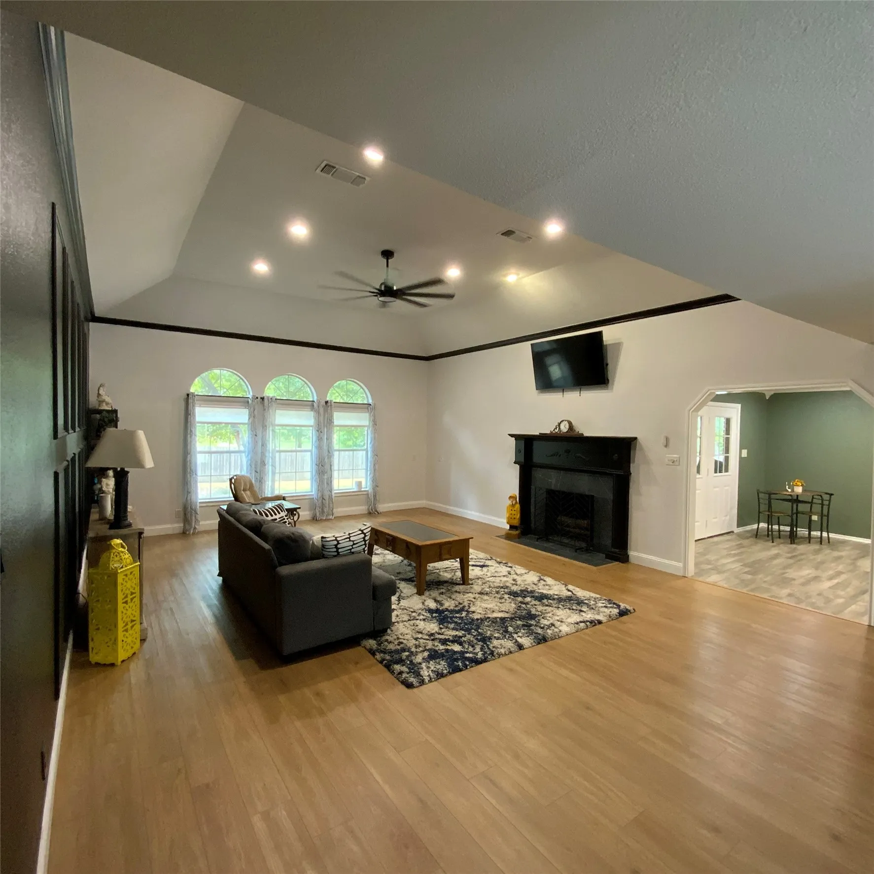 Vaulted ceiling with recessed lighting and a ceiling fan, wood-finish flooring, a black fireplace with a mantel, and three arched windows