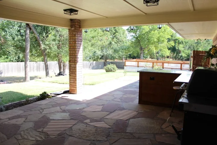 Covered patio featuring flagstone flooring, brick support column, and built-in outdoor cabinetry with a dark countertop