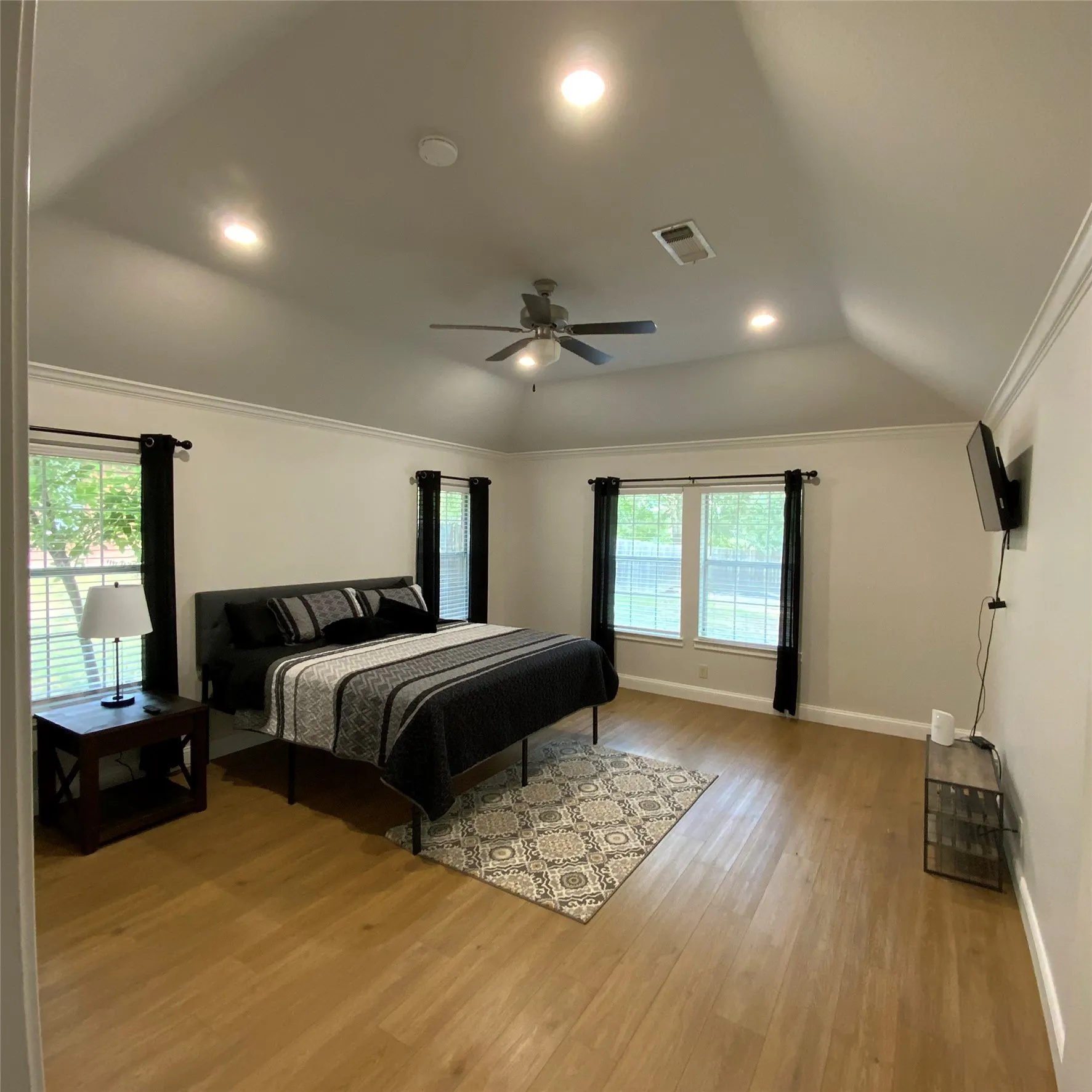 Vaulted ceiling with crown molding, recessed lighting, ceiling fan, wood-finish flooring, and multiple windows