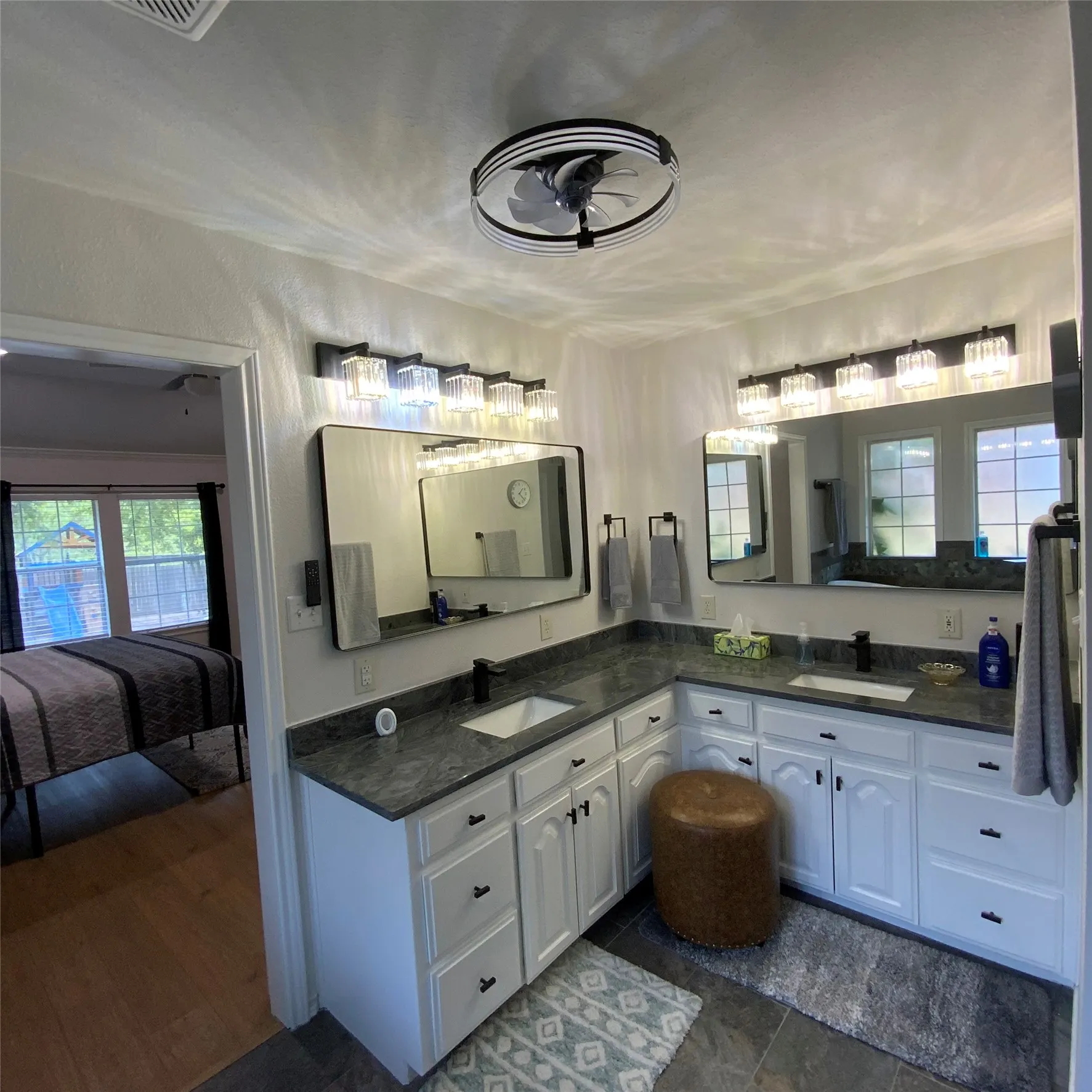 Dual vanity with dark countertops, white cabinetry, undermount sinks, and wall-mounted light fixtures