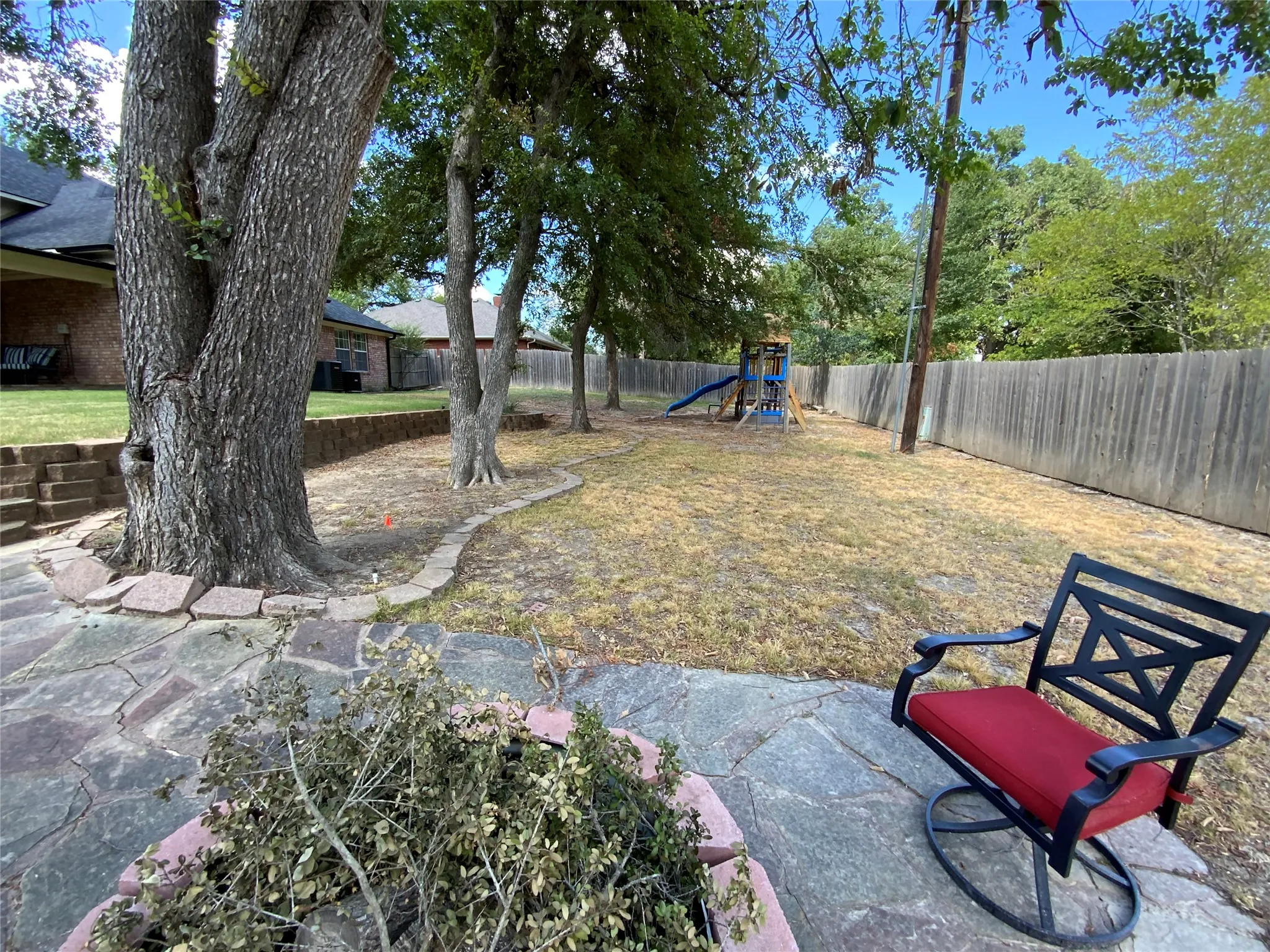 Expansive backyard featuring a natural stone patio, mature trees, a wooden privacy fence, and a terraced retaining wall