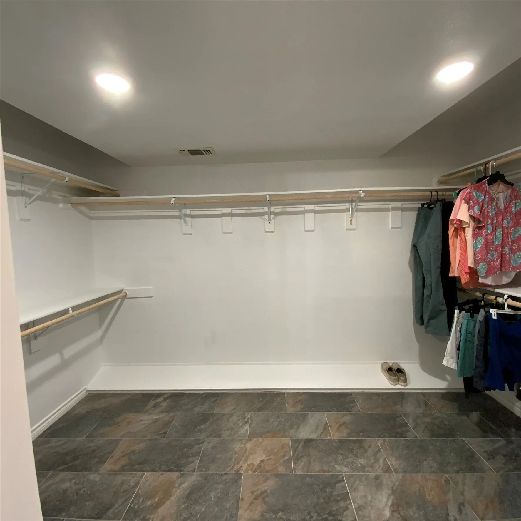Spacious closet with slate-style tile flooring, recessed lighting, and white wall-mounted shelving and hanging rods