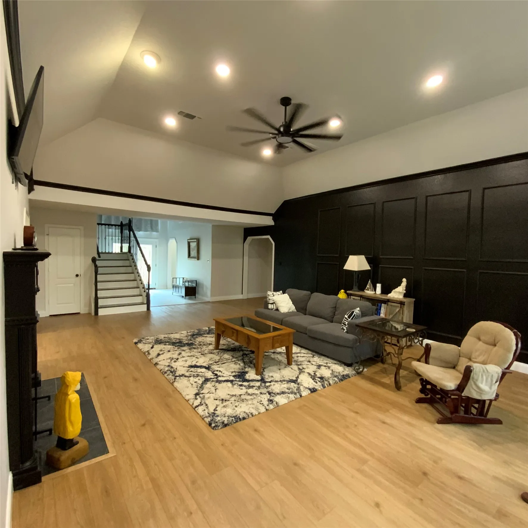 Vaulted ceilings with recessed lighting, wood-finish flooring, a built-in electric fireplace, and a wainscoting accent wall