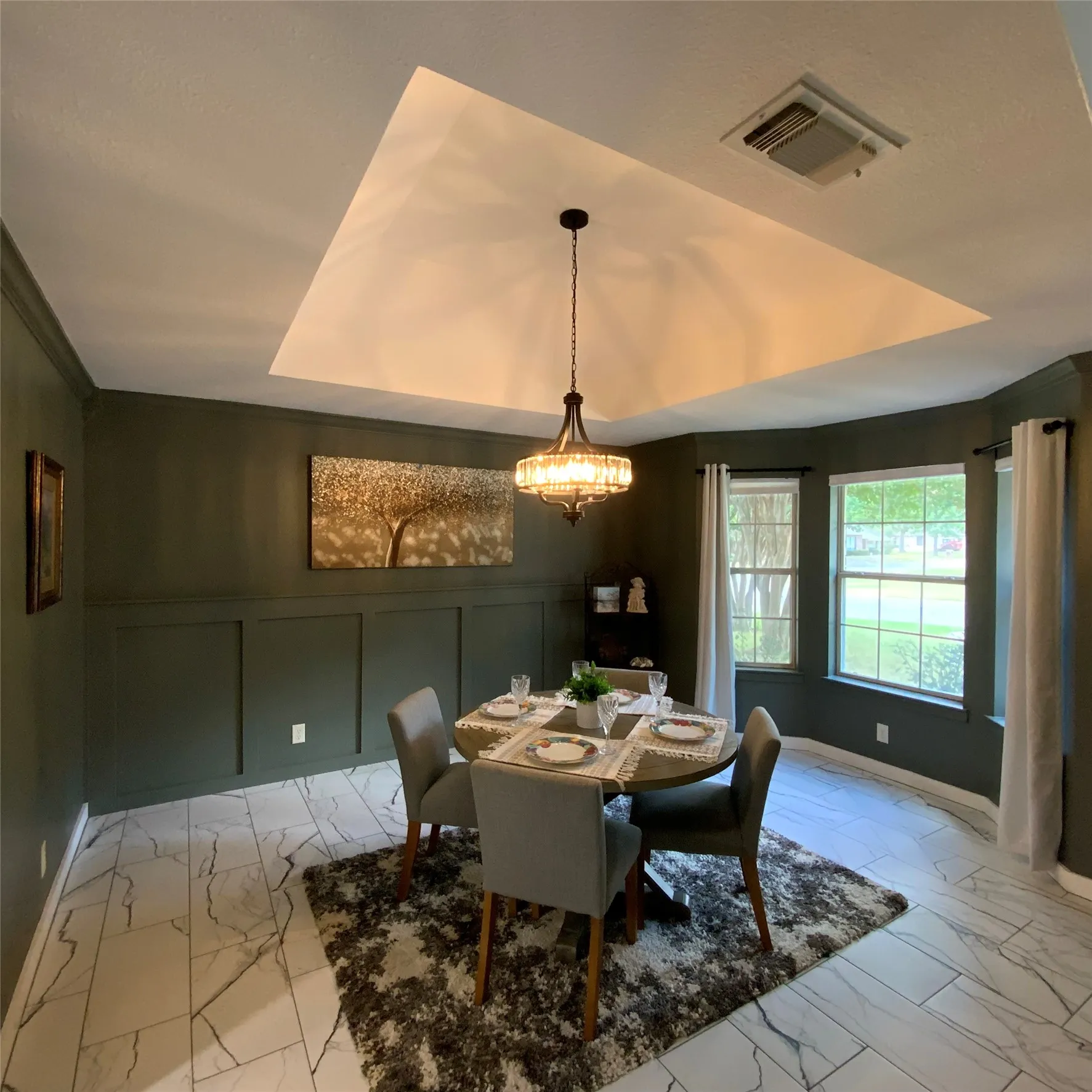 Tray ceiling with a decorative chandelier, board and batten wall detailing, and large windows