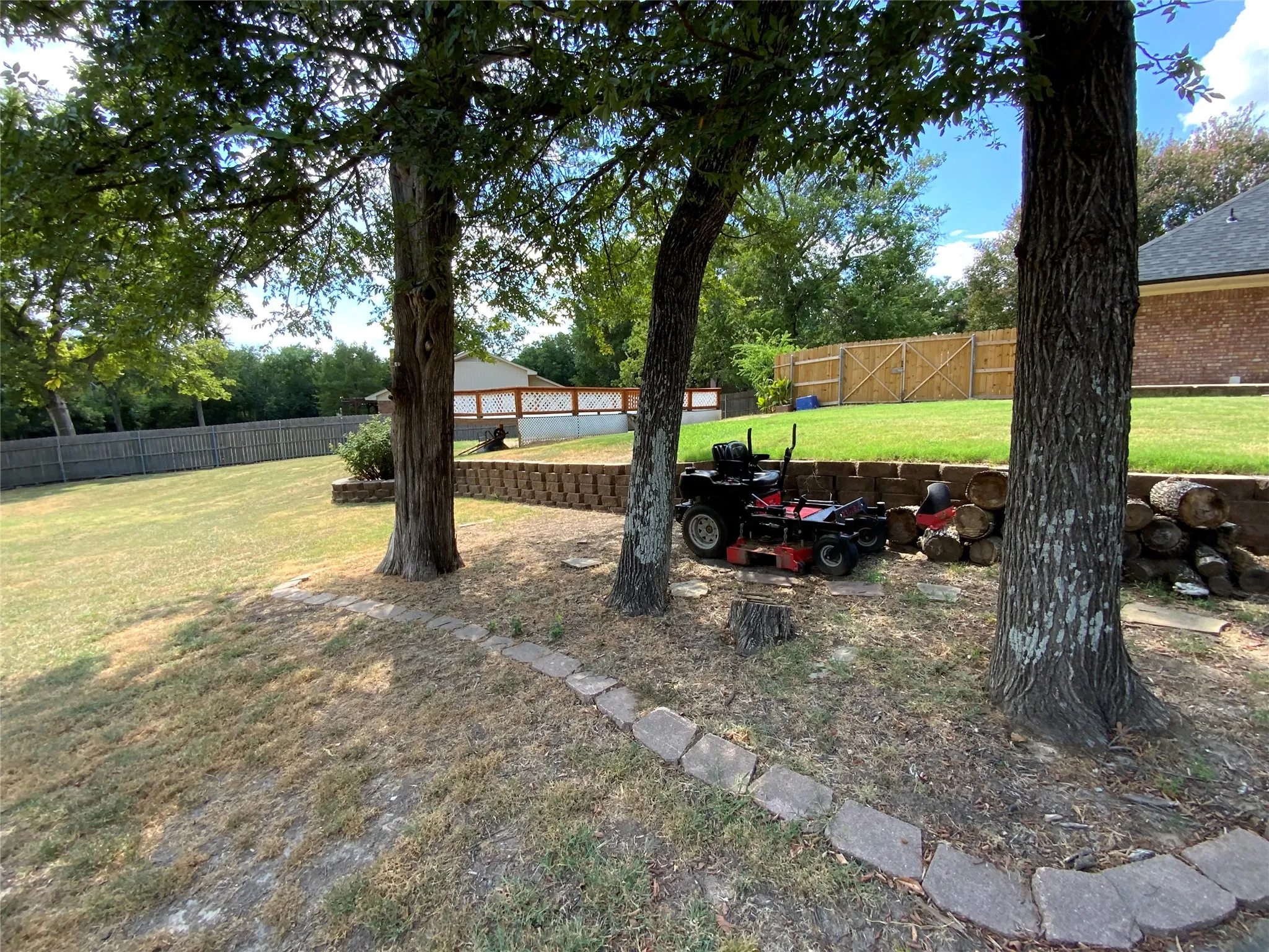 Expansive outdoor area featuring mature trees, a wooden privacy fence, and a tiered retaining wall