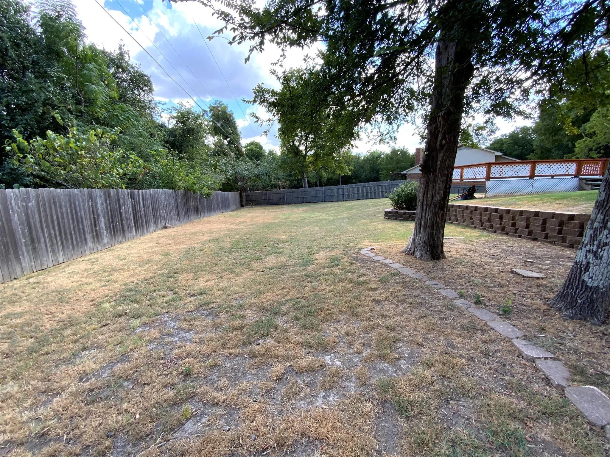 Expansive yard featuring mature trees, a wood privacy fence, and a retaining wall