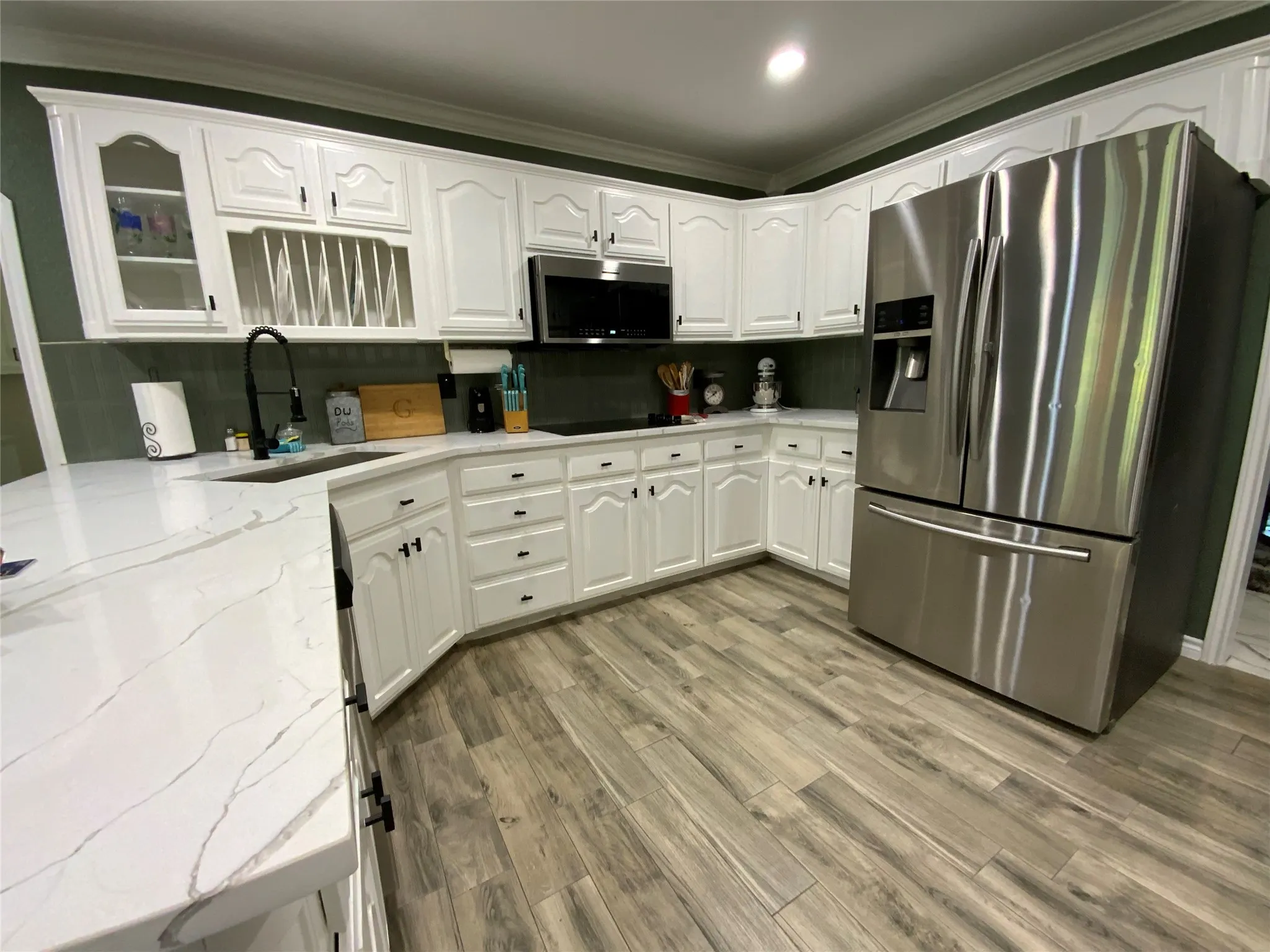White cabinetry with dark hardware, stainless steel refrigerator, white countertops, dark subway tile backsplash, and wood-finish flooring
