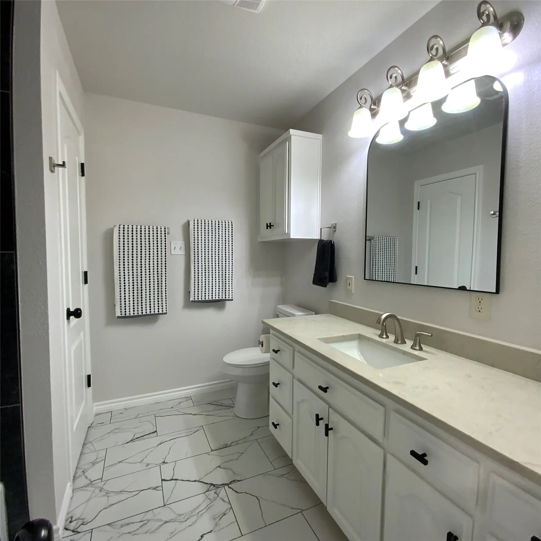 White vanity with matte black hardware, single undermount sink, and a light-colored countertop