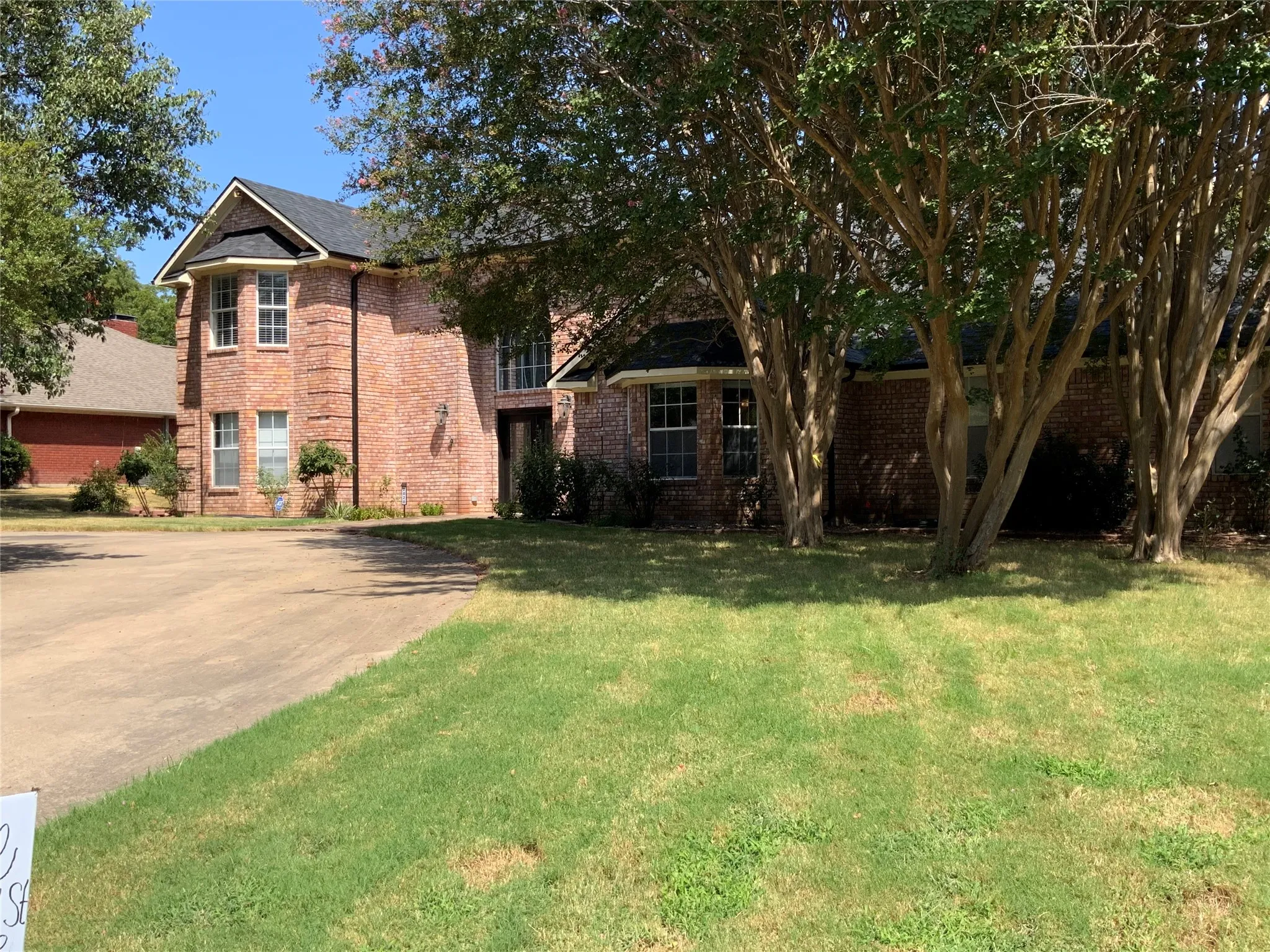 Brick exterior, gabled roofline, bay window, mature trees, and a paved driveway