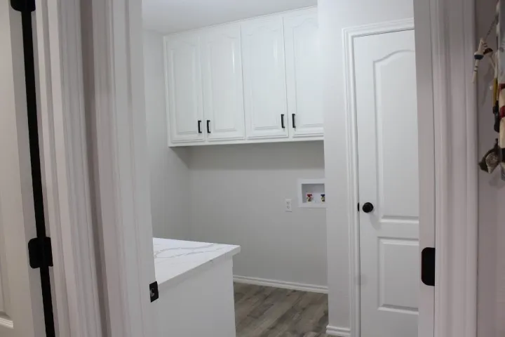 White shaker-style cabinetry, white quartz-finish countertop, wood-finish flooring, and a panel door with black hardware